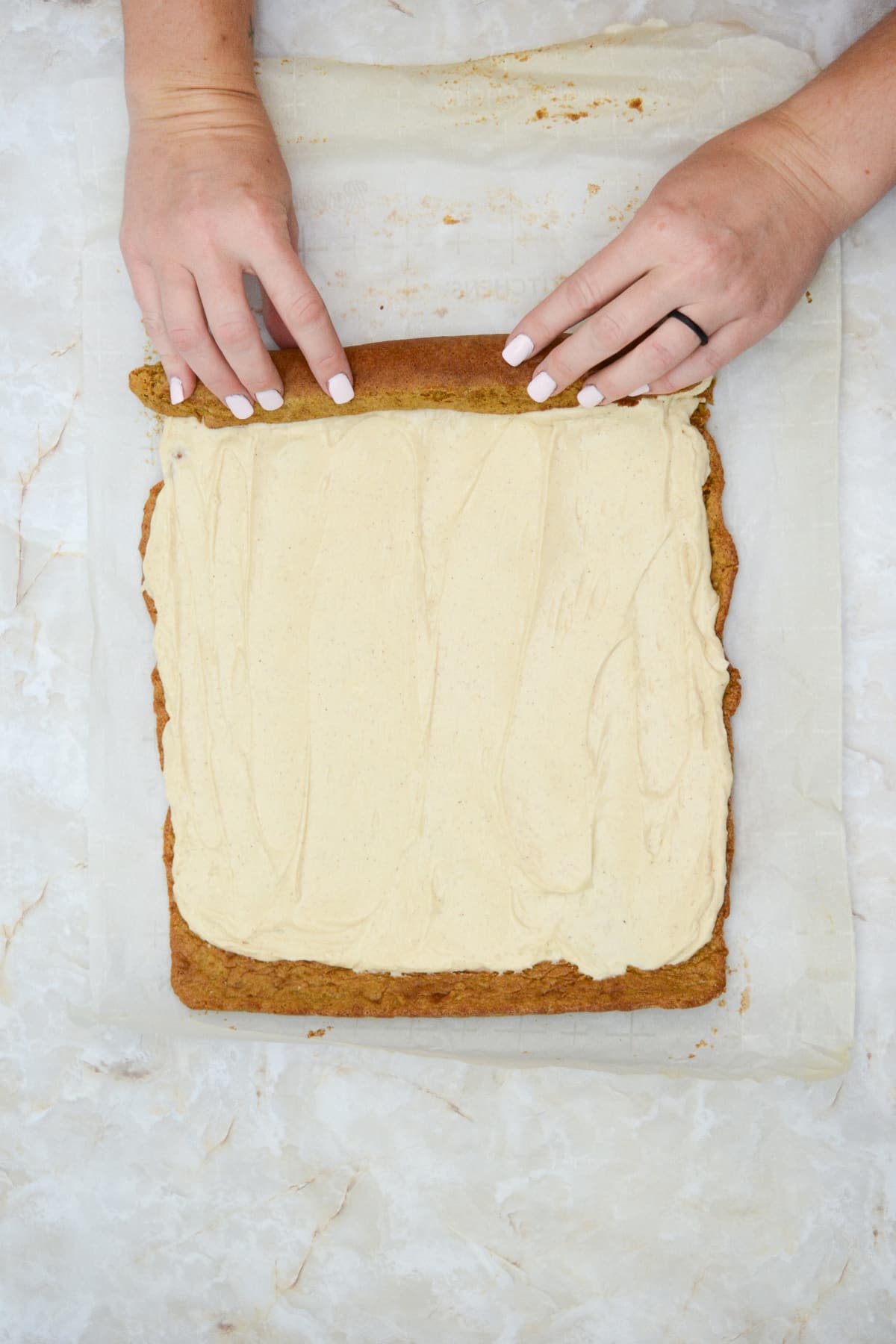 frosting added to a gingerbread cake, and it's being rolled on parchment paper.