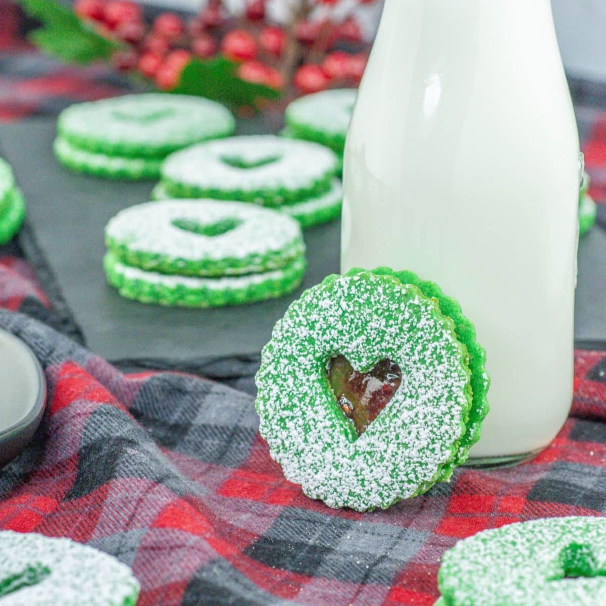 grinch linzer cookie leaning against a glass of milk.