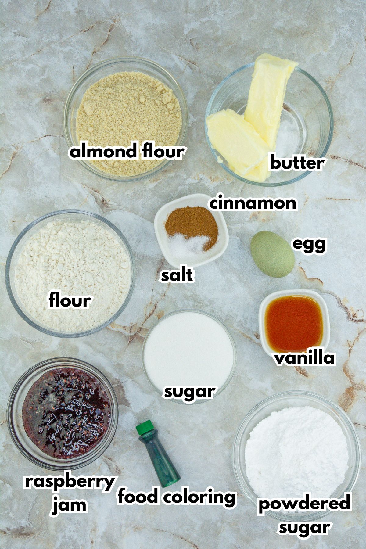 bowls of almond flour, butter, flour, ground cinnamon, salt, egg, raspberry jam, food coloring, sugar, vanilla extract and powdered sugar.