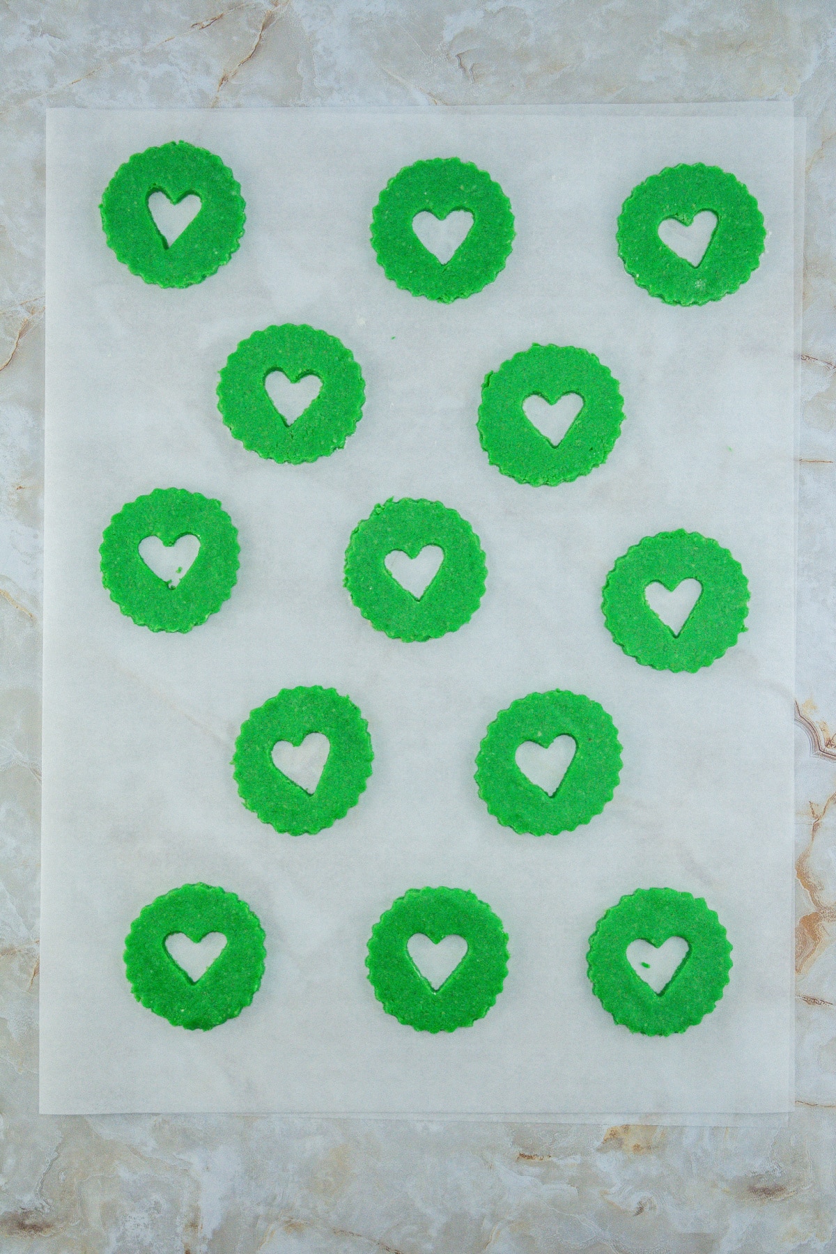 green cookie dough with small hearts cut out on a piece of parchment paper.