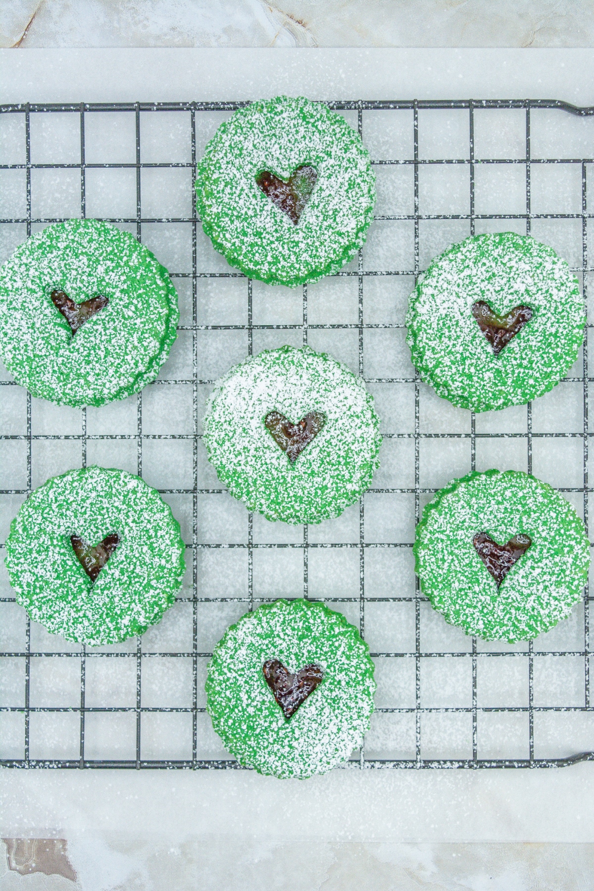 grinch linzer cookies being dusted on powdered sugar on a wire cooling rack.