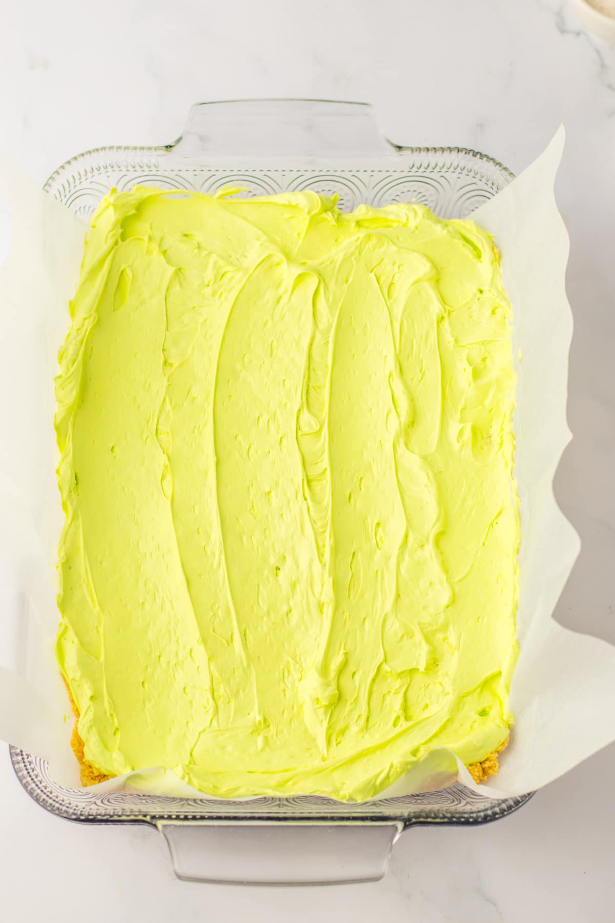 green cream cheese on top of a cookie crust in a glass baking dish.