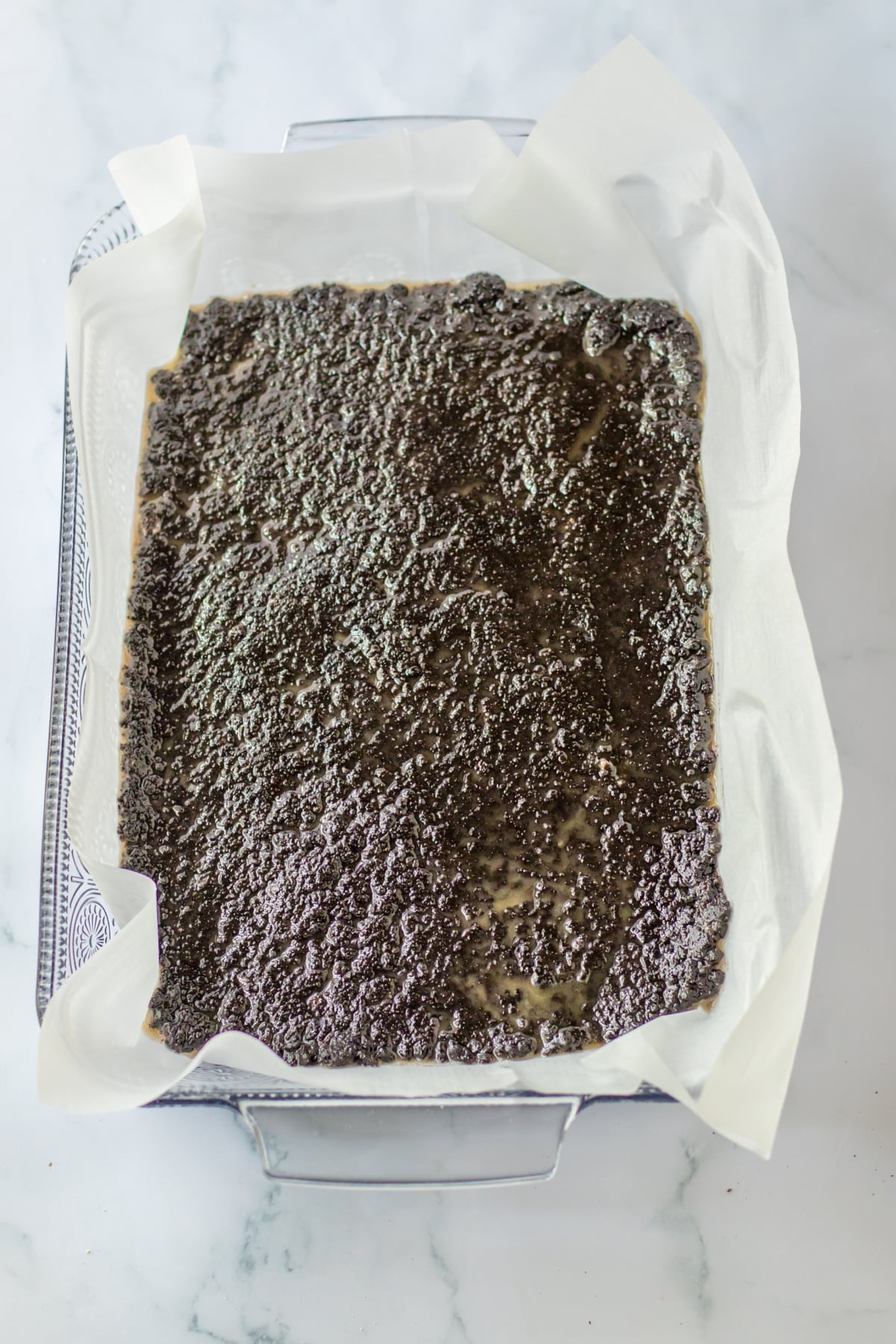 oreo cookie crust being spread in a parchment lined glass baking dish.