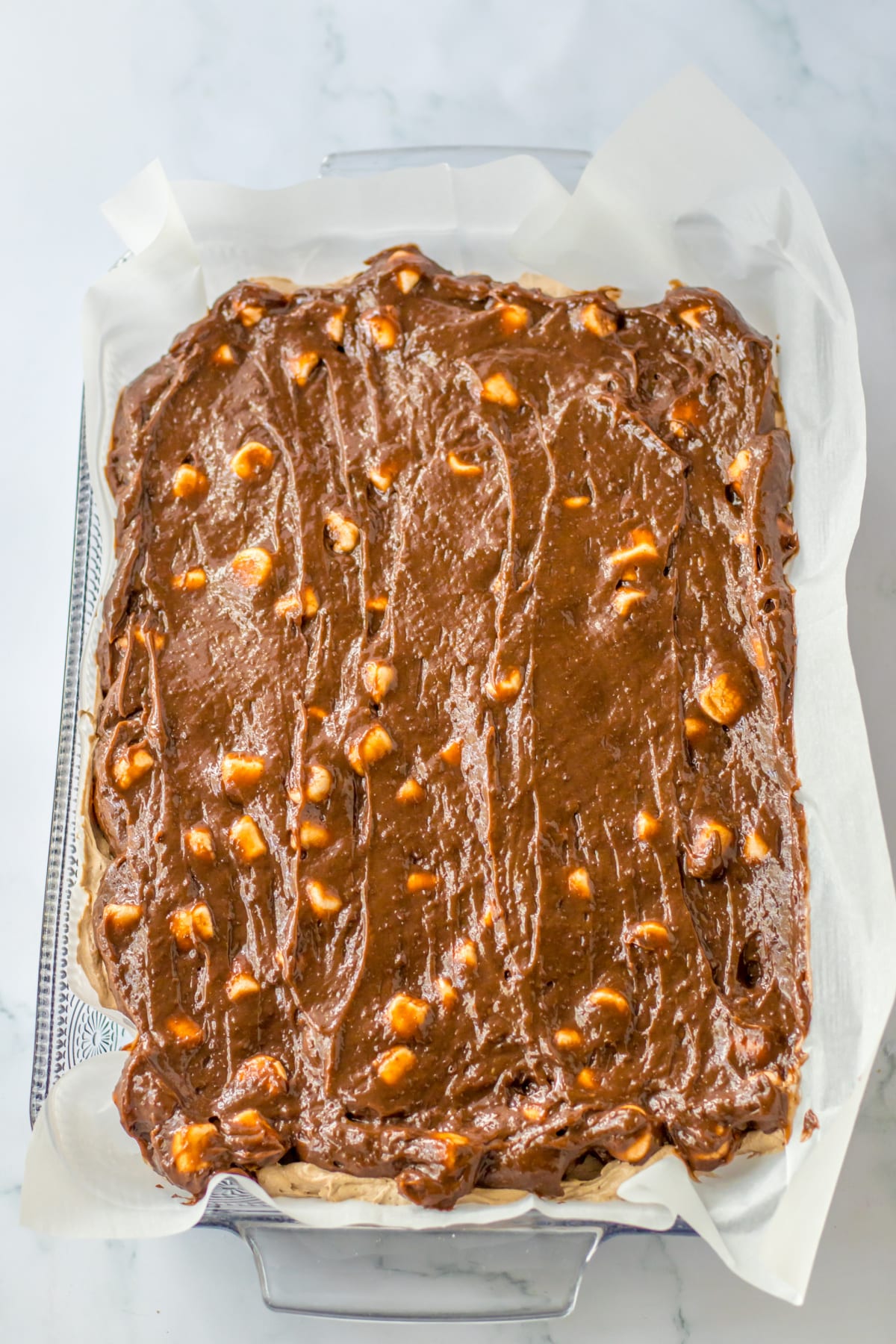 chocolate pudding layer being spread on top of the dessert in a glass baking dish.