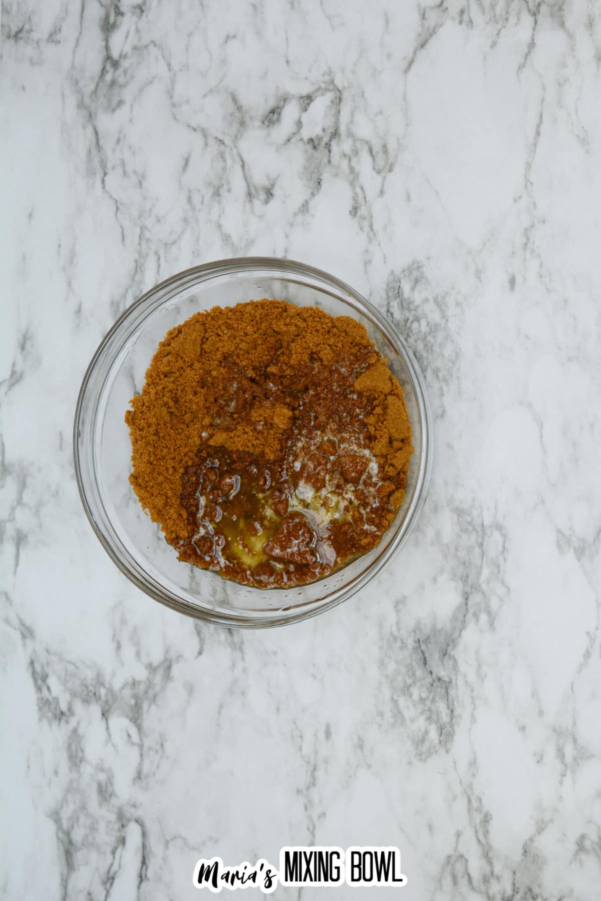 crushed biscoff cookies and melted butter being mixed in a small glass bowl.