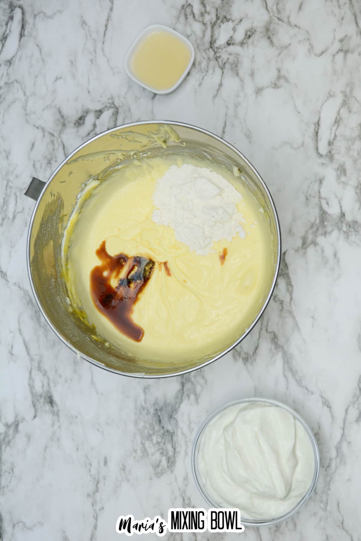 vanilla extract and flour being added to cheesecake batter.