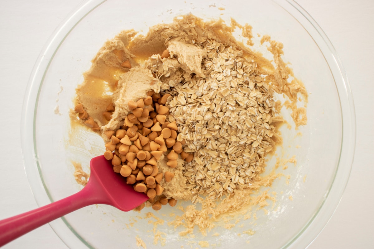 oatmeal and butterscotch being mixed into a cookie dough in a glass bowl.