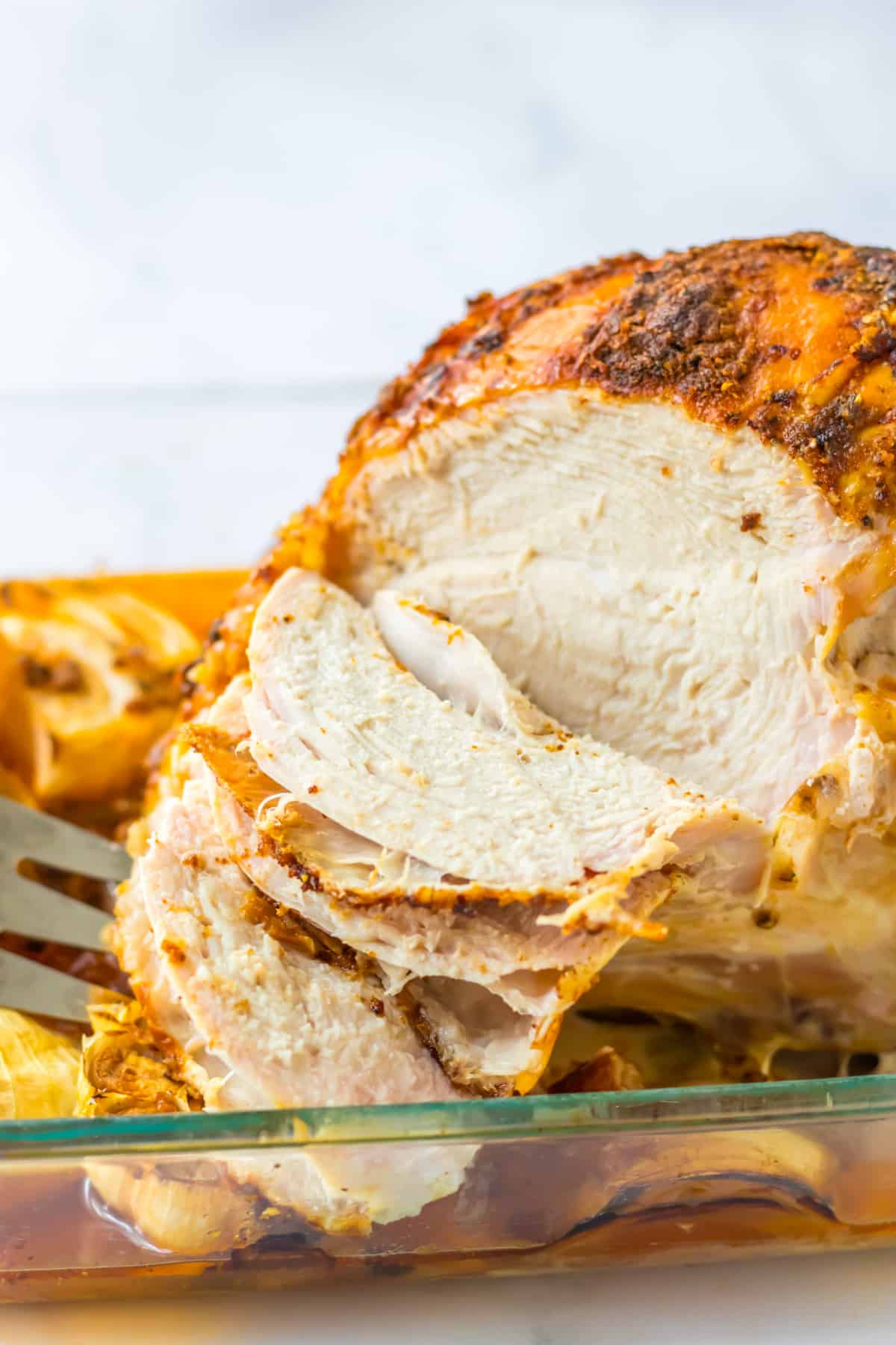 oven roasted turkey breast being sliced in a glass baking dish.