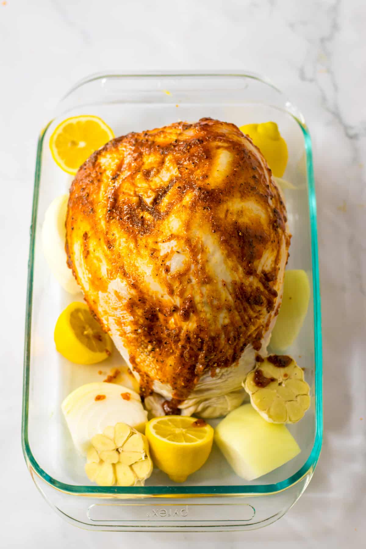 turkey breast being seasoned in a glass baking dish with lemons and garlic.