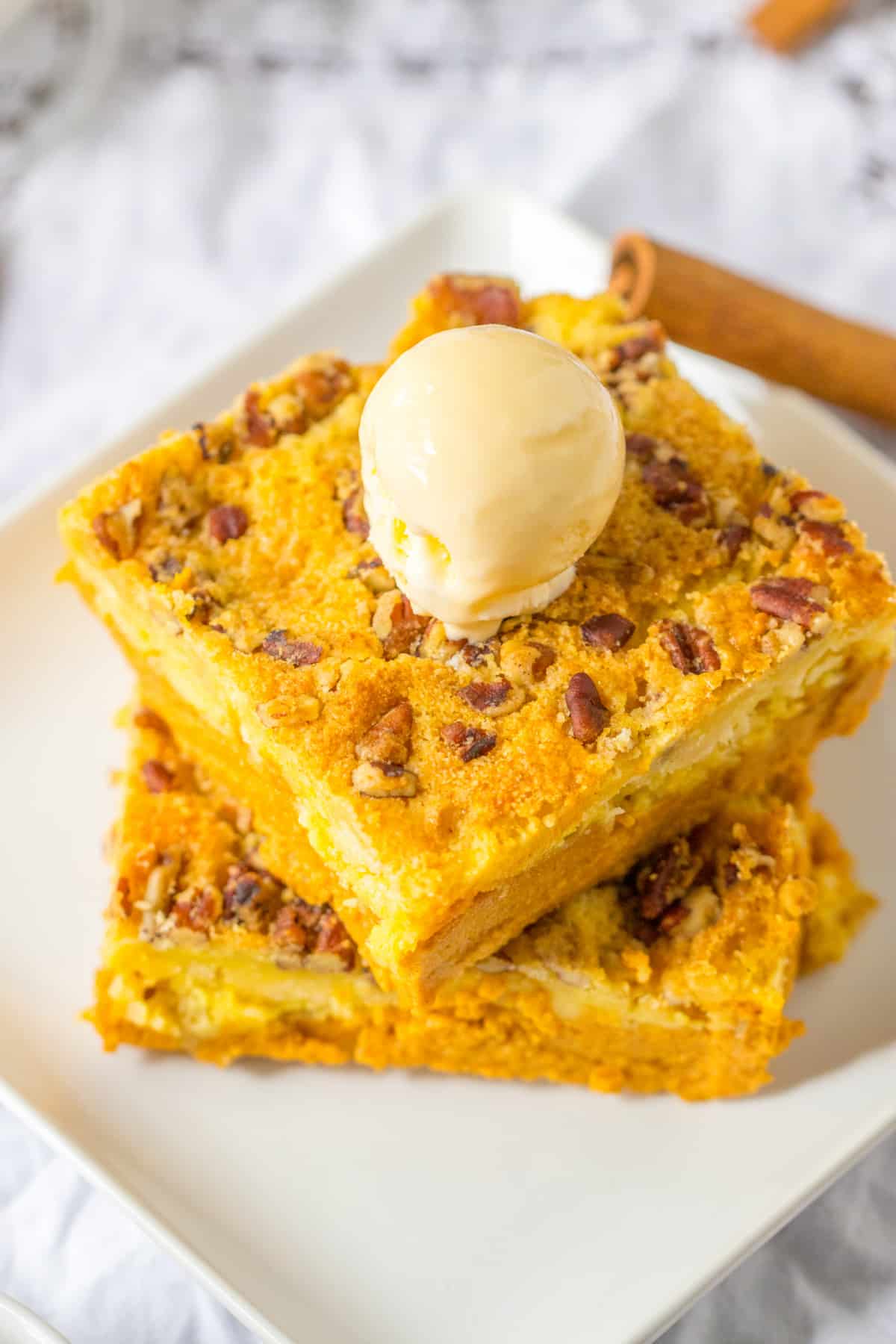 two slices of pumpkin crunch dump cake stacked on a plate with a scoop of ice cream on top.