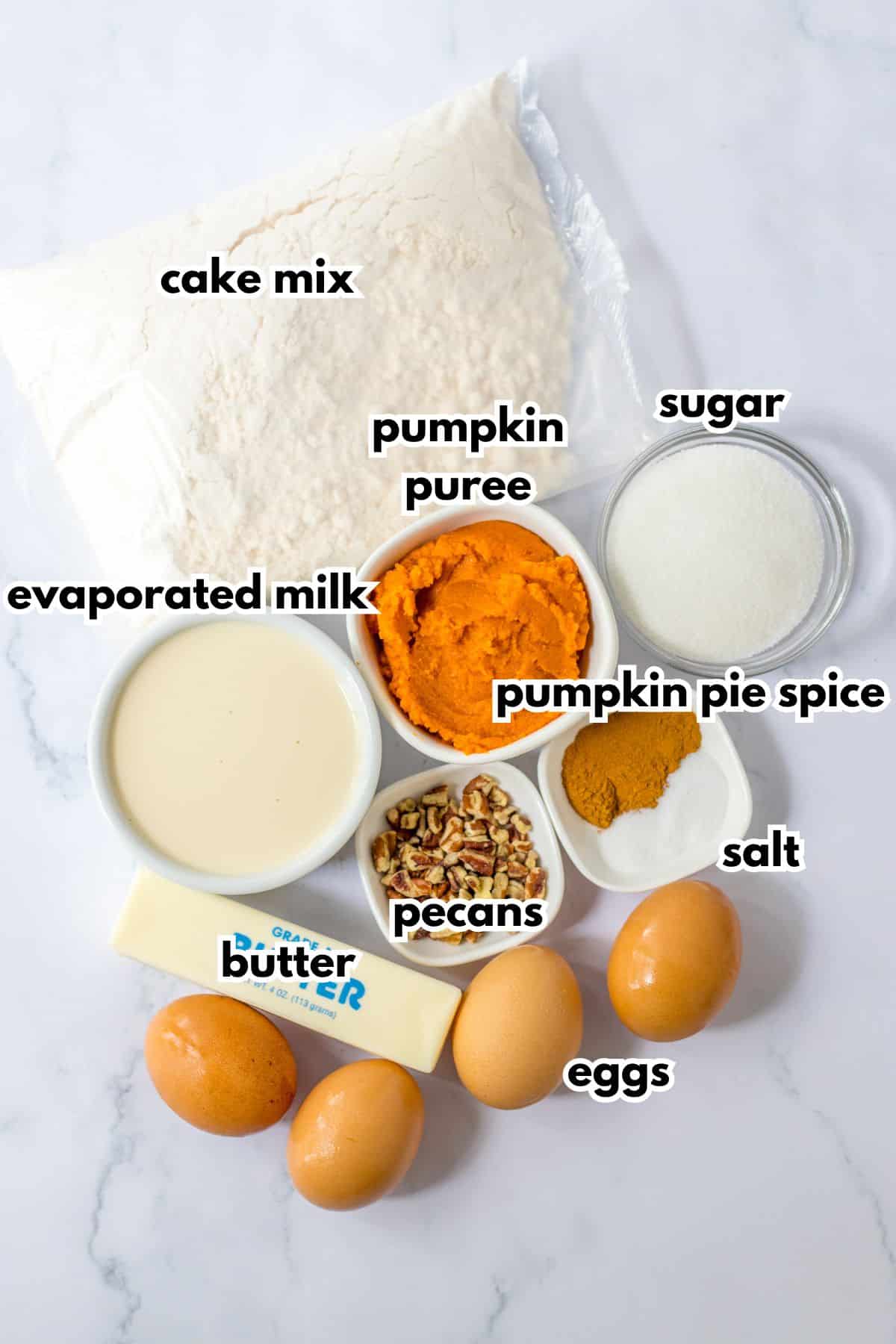 bag of cake mix, bowls of pumpkin puree, sugar, evaporated milk, pumpkin pie spice, pecans, salt, butter, and eggs on a counter.
