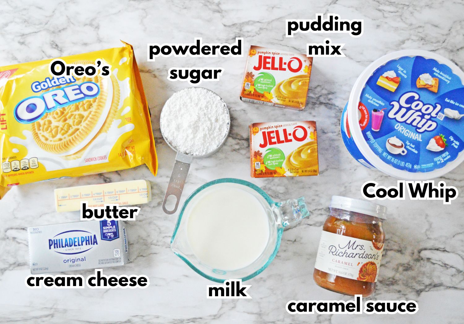 Golden Oreo's, powdered sugar, pudding mix, butter, cream cheese, milk, caramel sauce, and Cool Whip on a marble counter.