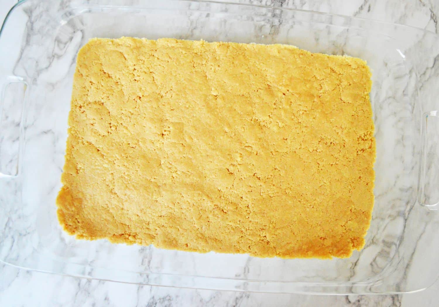 vanilla oreo cookie crust being pressed into a glass baking dish.