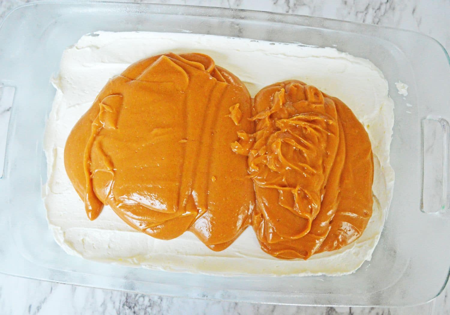 pumpkin layer being spread on top of a cream cheese layer in a glass baking dish.