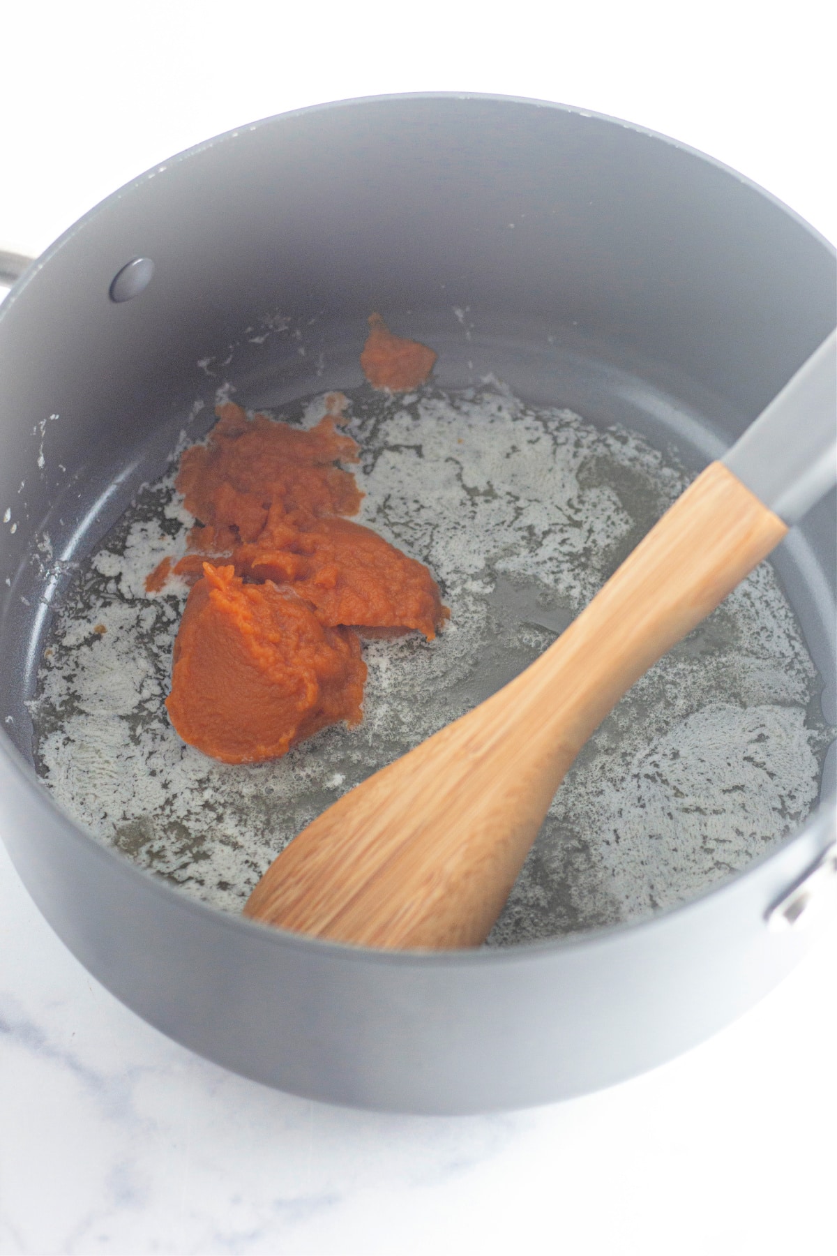 melted butter and pumpkin puree being mixed in a large pot with a wooden spoon.