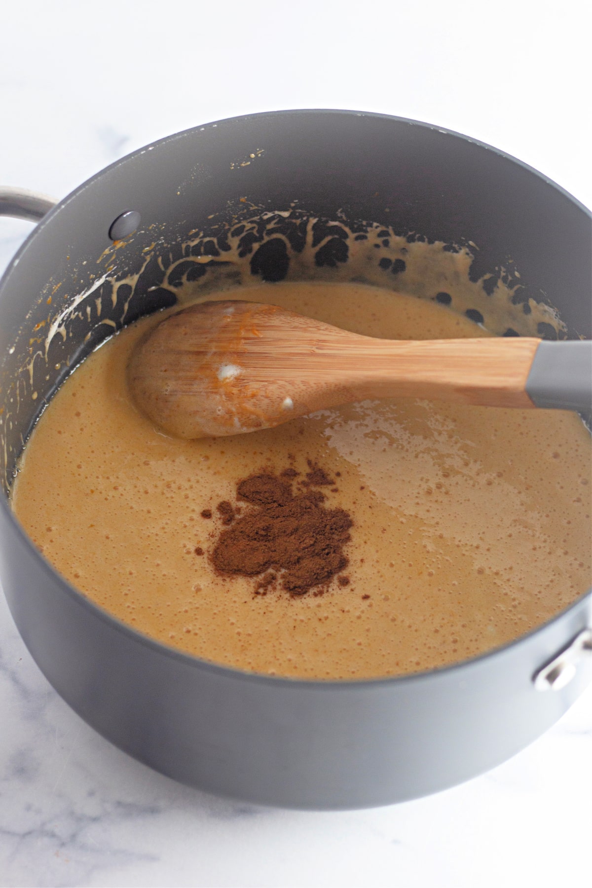 pumpkin spice being added to melted marshmallows in a large pot.
