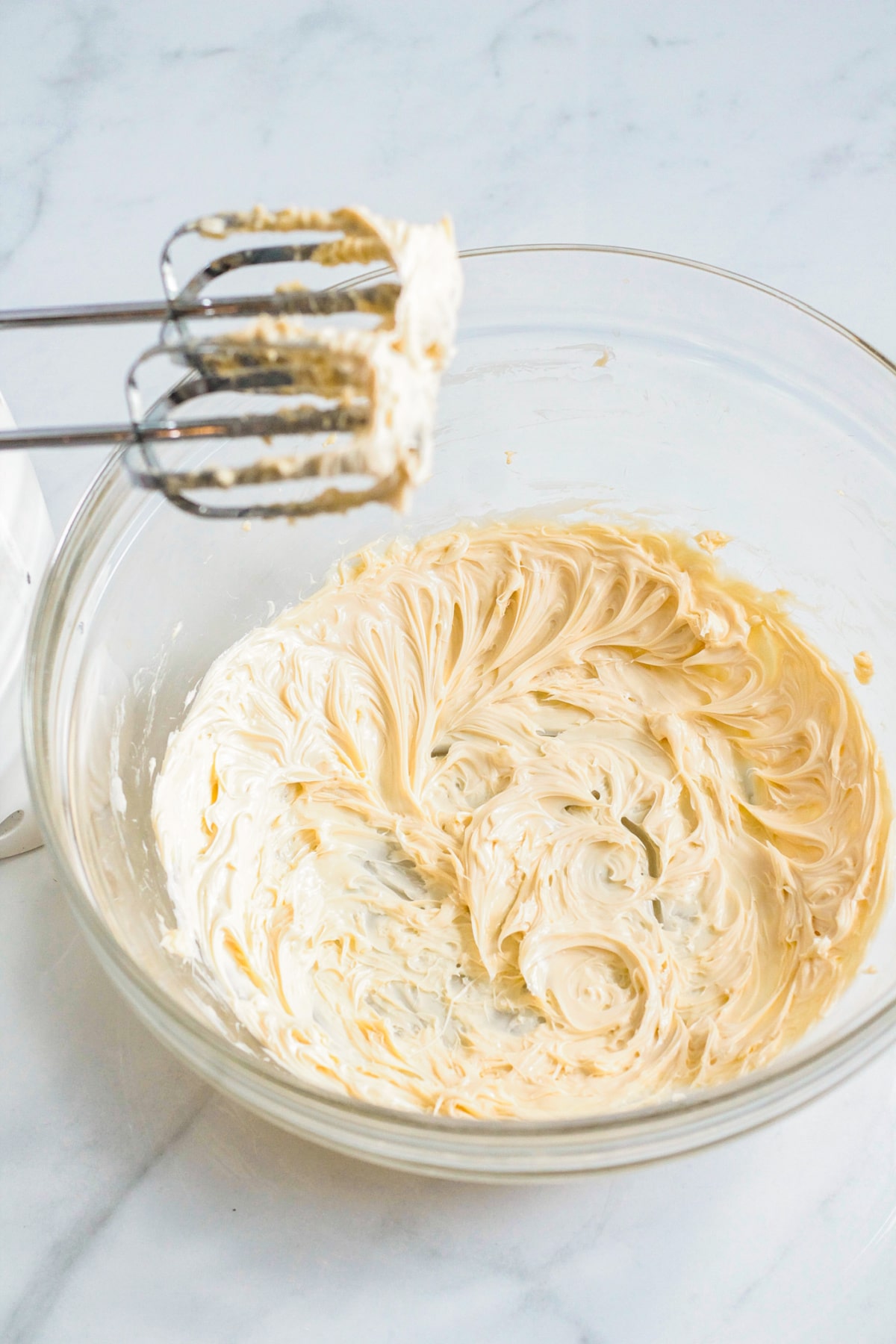 butter cream frosting being mixed in a glass mixing bowl with a hand mixer.
