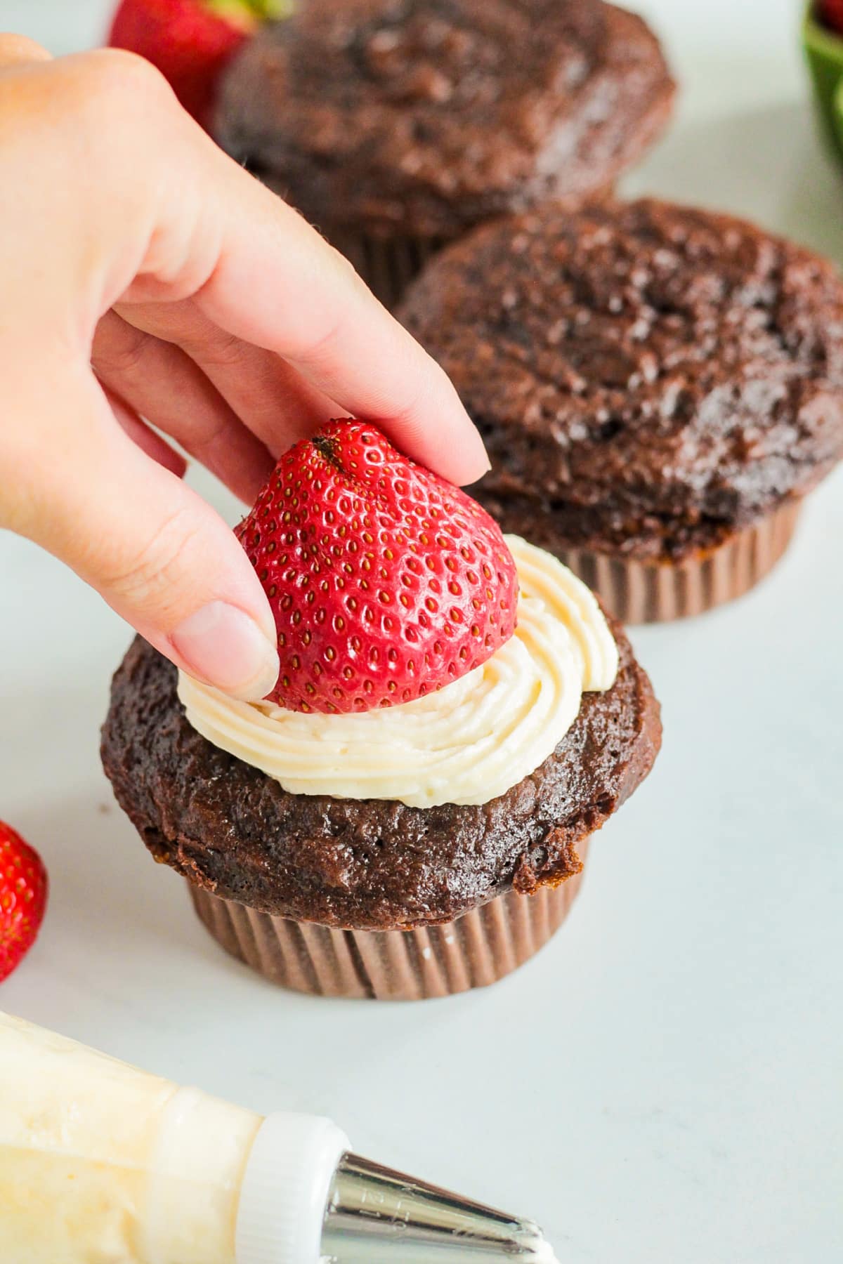 strawberry being added to the top of a frosting cupcake.