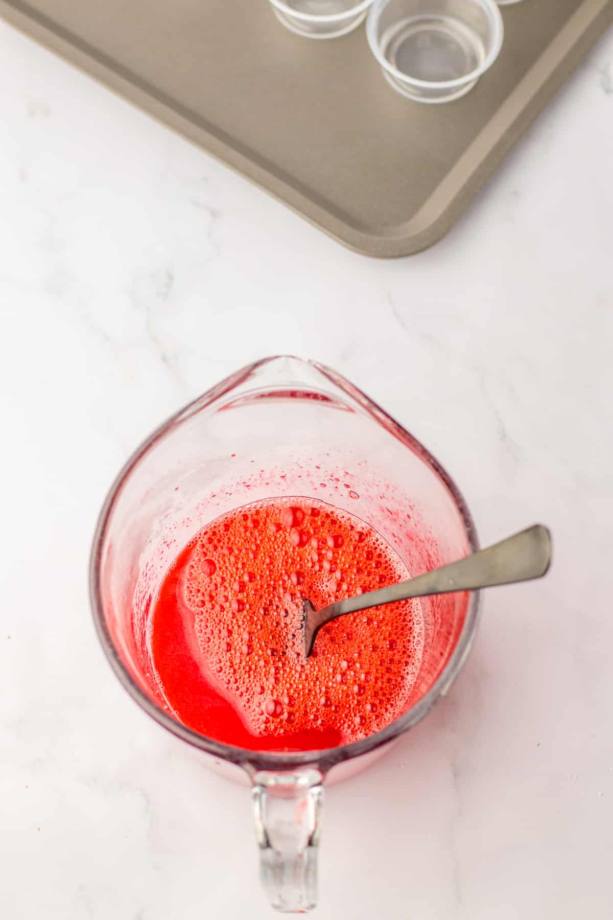 strawberry jello being mixed with water in a measuring cup.