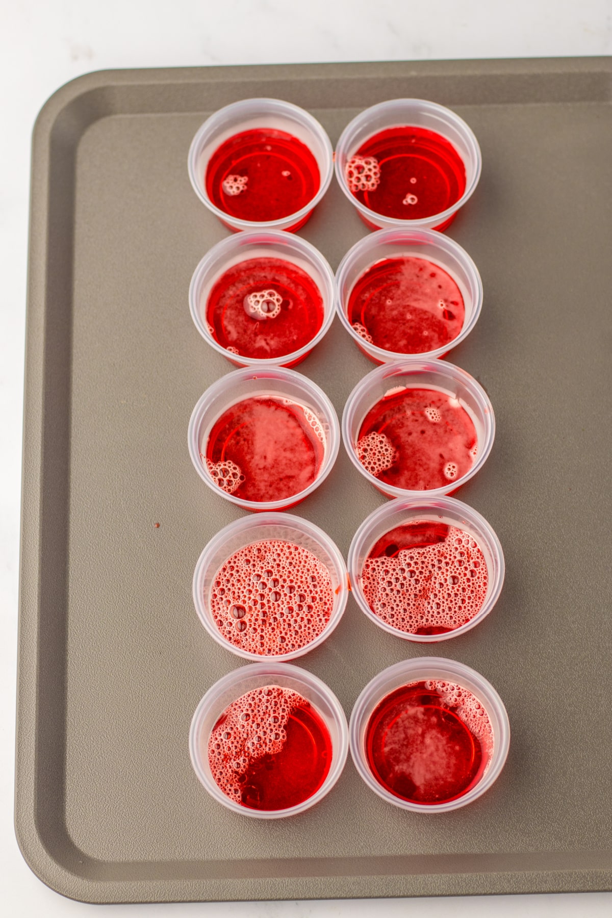 strawberry jello cooling in plastic shot cups on a baking sheet.