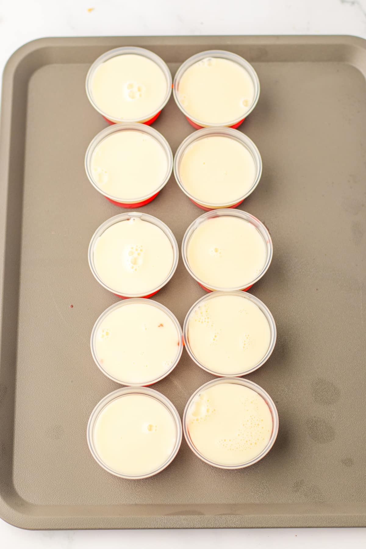 sweetened condensed milk being added to the top of plastic shots.
