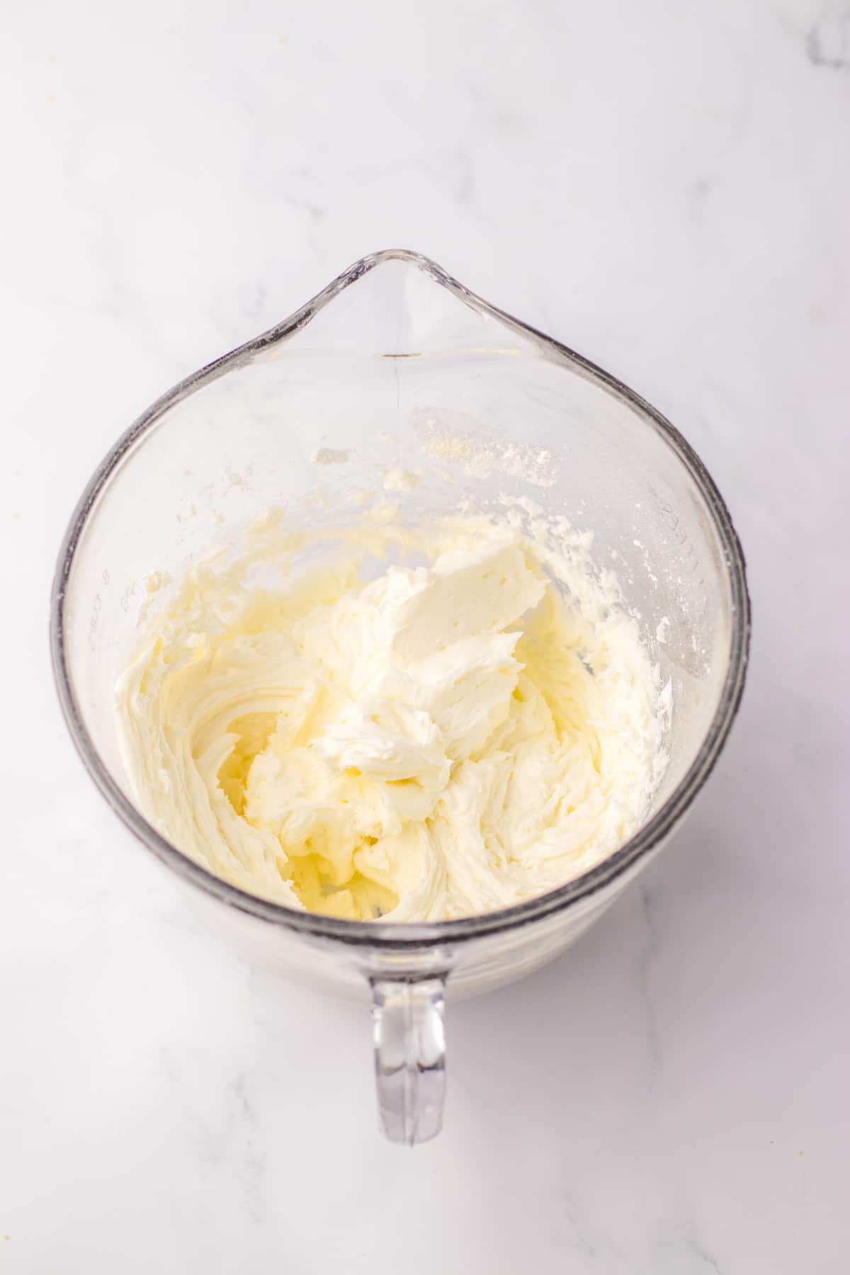 buttercream frosting being mixed in a large glass mixing bowl.