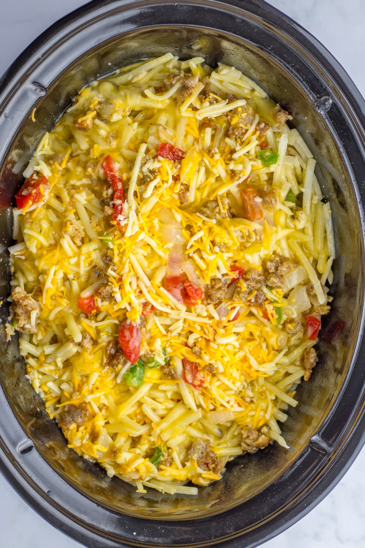 eggs and cheese being added on top of a casserole in the slow cooker.