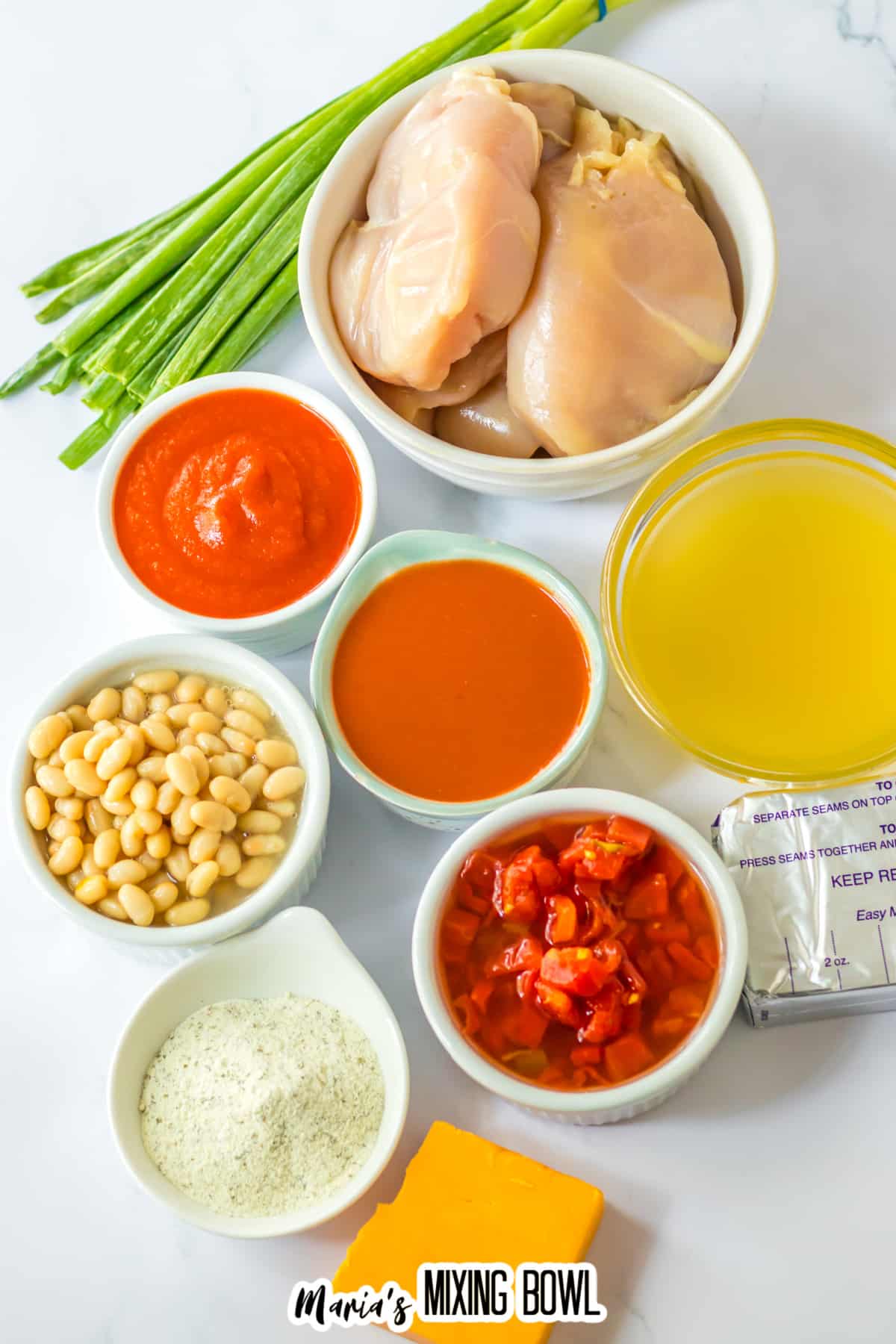 bowls of raw chicken breasts, green onions, buffalo sauce, tomato sauce, chicken broth, white beans, diced tomatoes, ranch seasoning, cream cheese, and cheddar cheese.