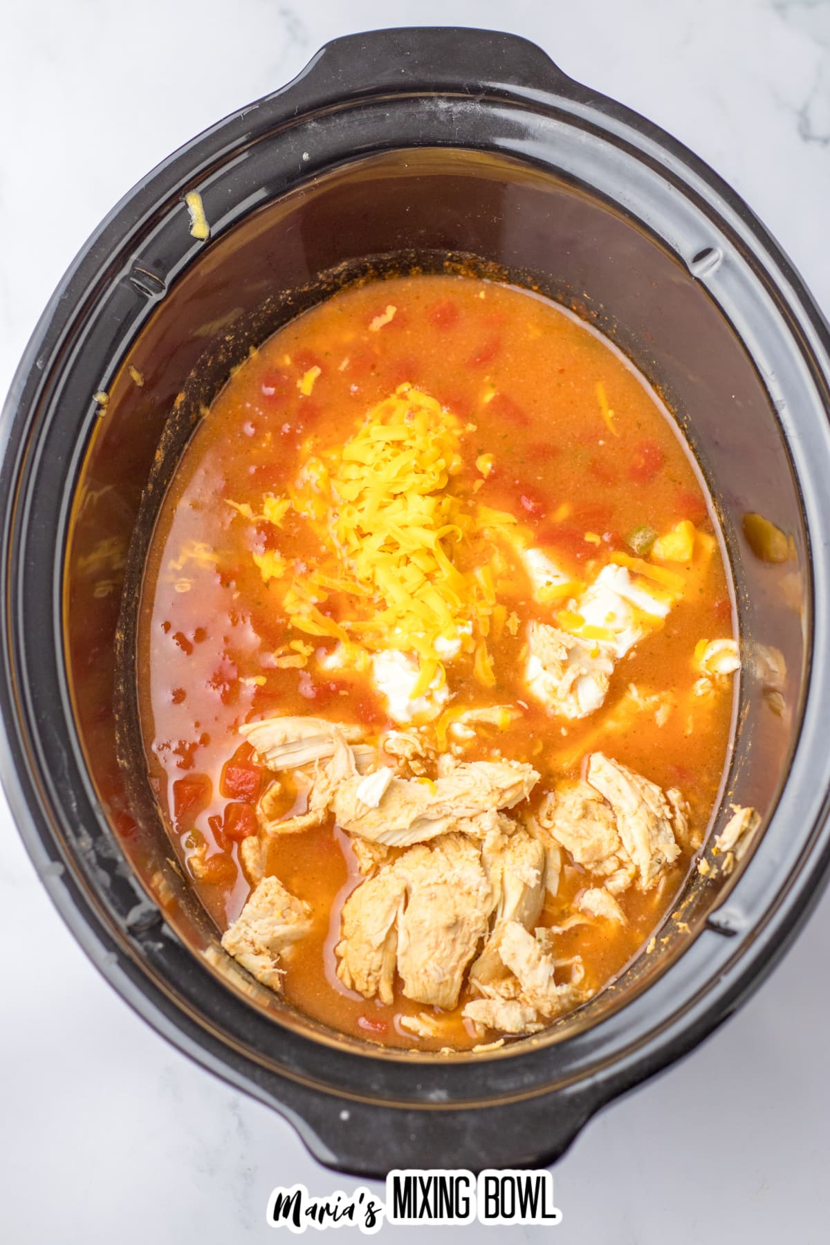 chicken and cheese being added to buffalo chicken chili in the slow cooker.