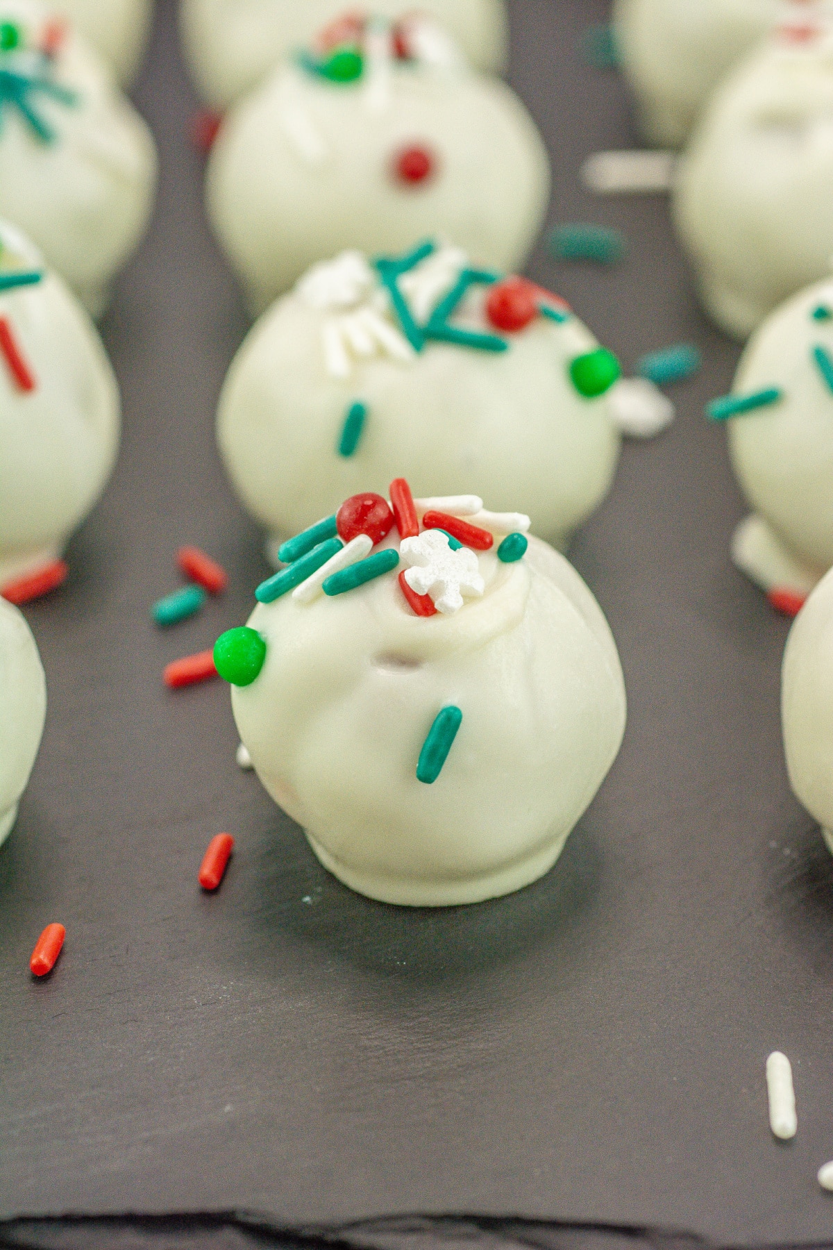 sugar cookie truffles topped with sprinkles on a cutting board.