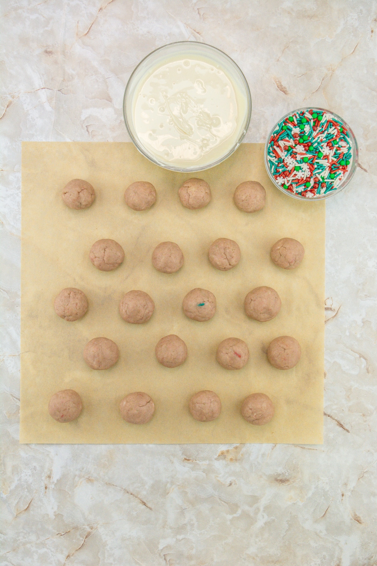 a bowl of melted white chocolate and a piece of parchment paper filled with sugar cookie truffles.