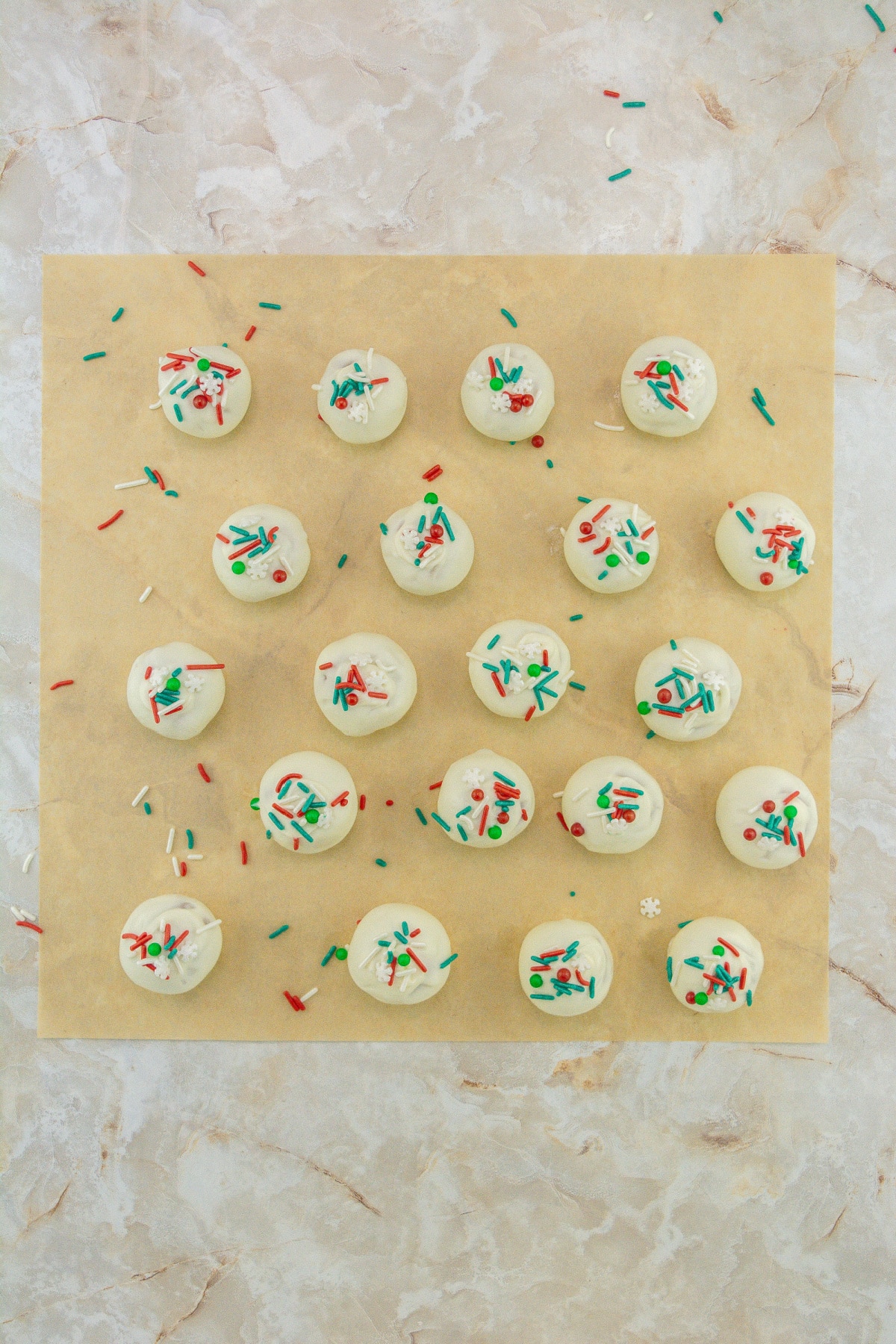 sprinkles being added to the top of sugar cookie truffles on parchment paper.