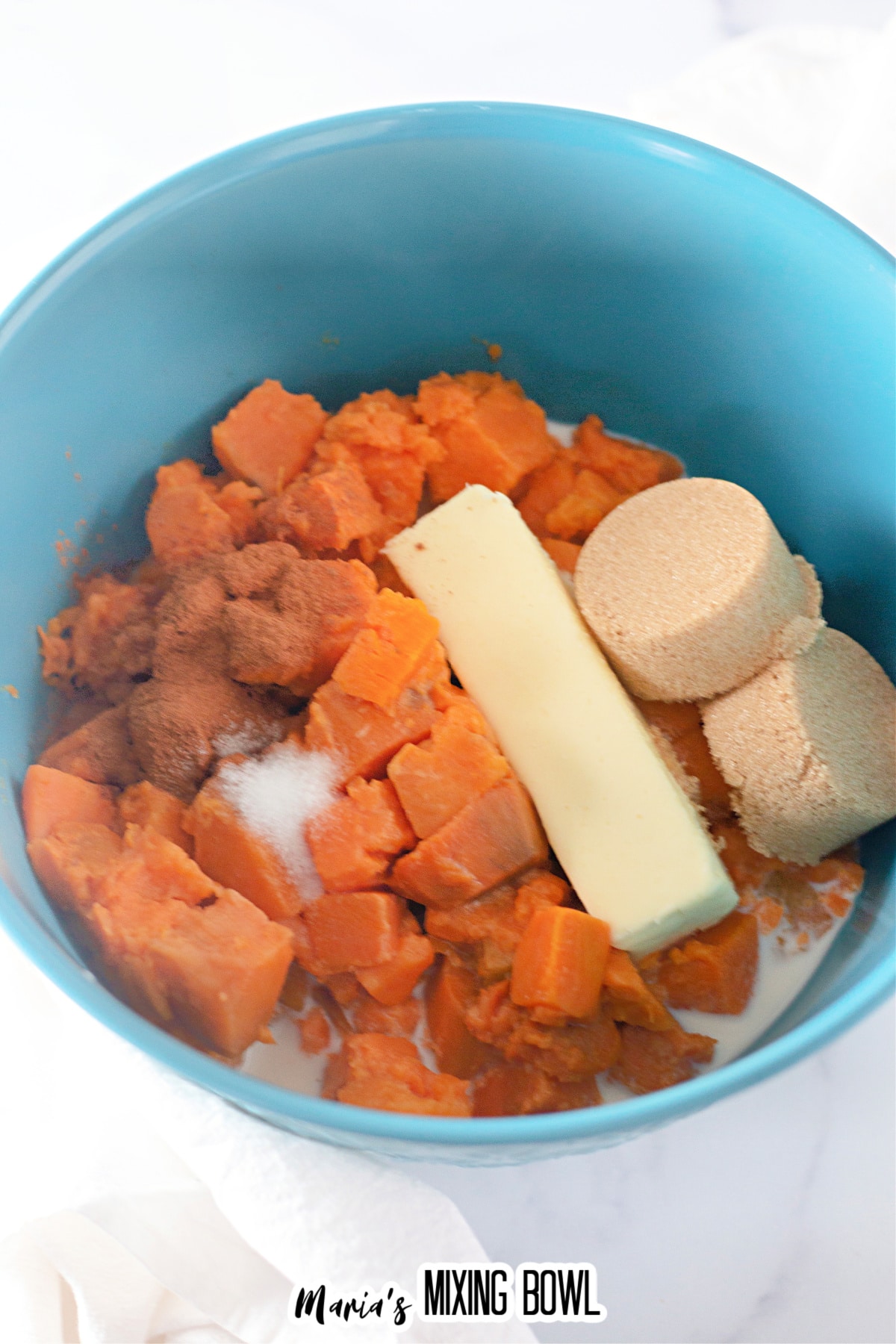 Bowl of cooked sweet potatoes, butter, brown sugar, and cinnamon about to be whipped.