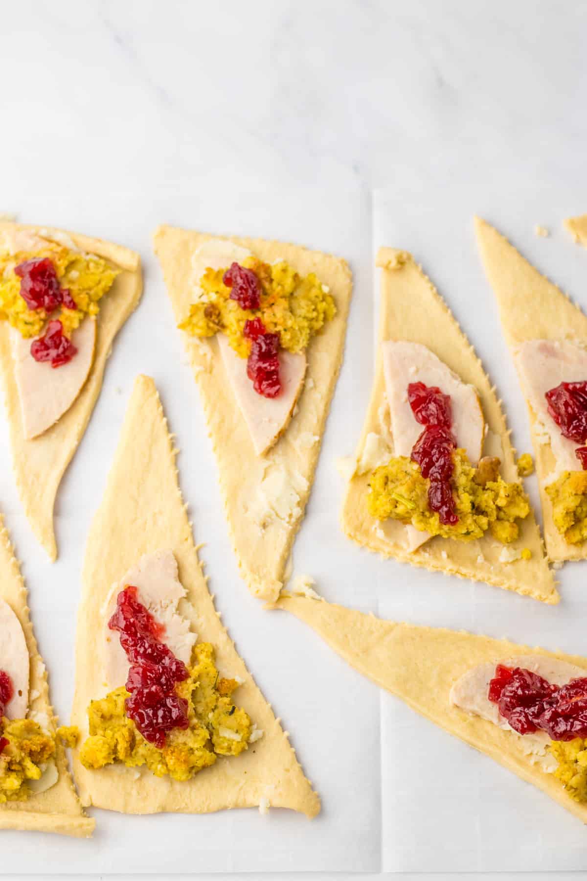 raw crescent rolls being topped with mashed potatoes, turkey, stuffing and cranberry.