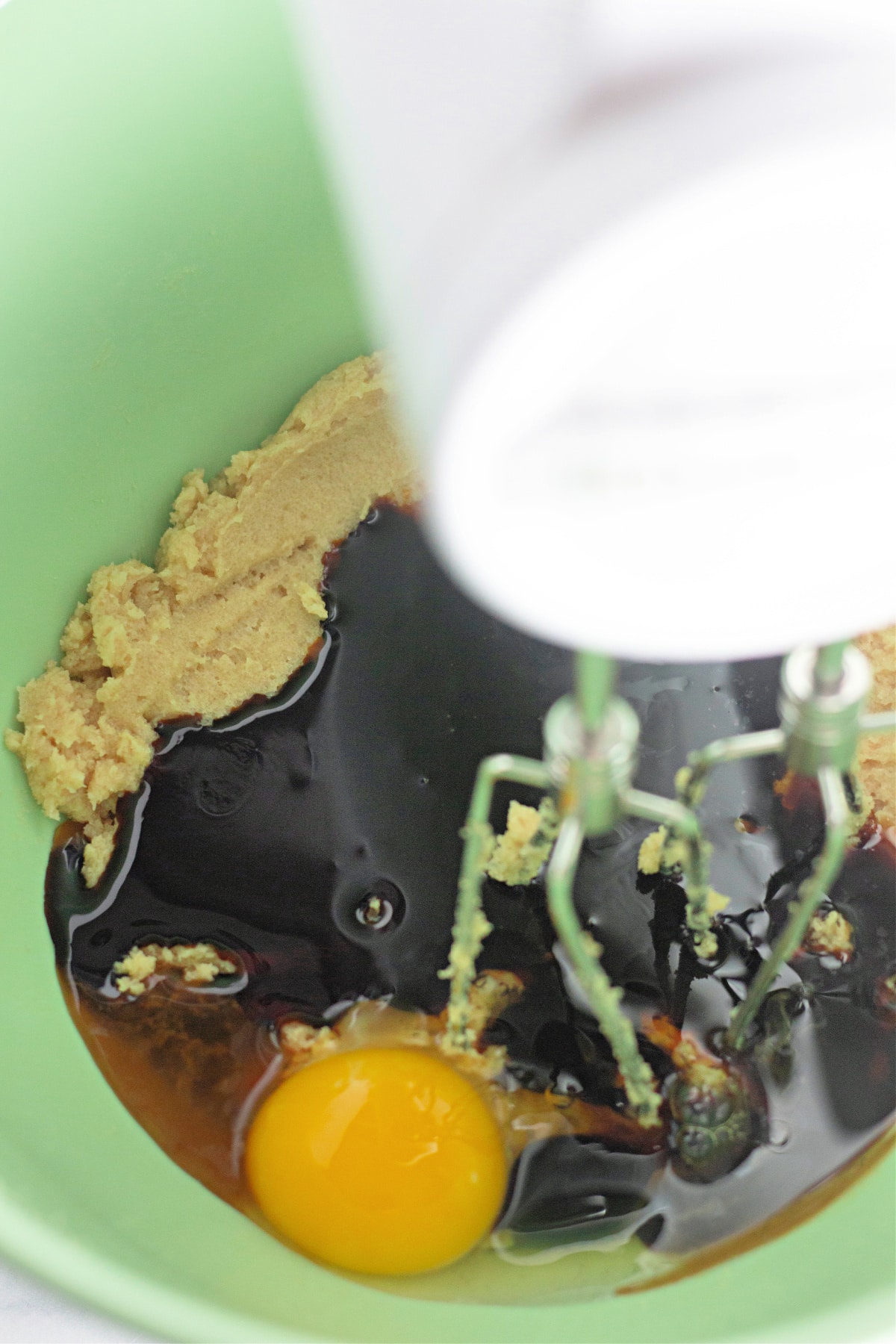 wet ingredients being mixed with a hand mixer in a mixing bowl.