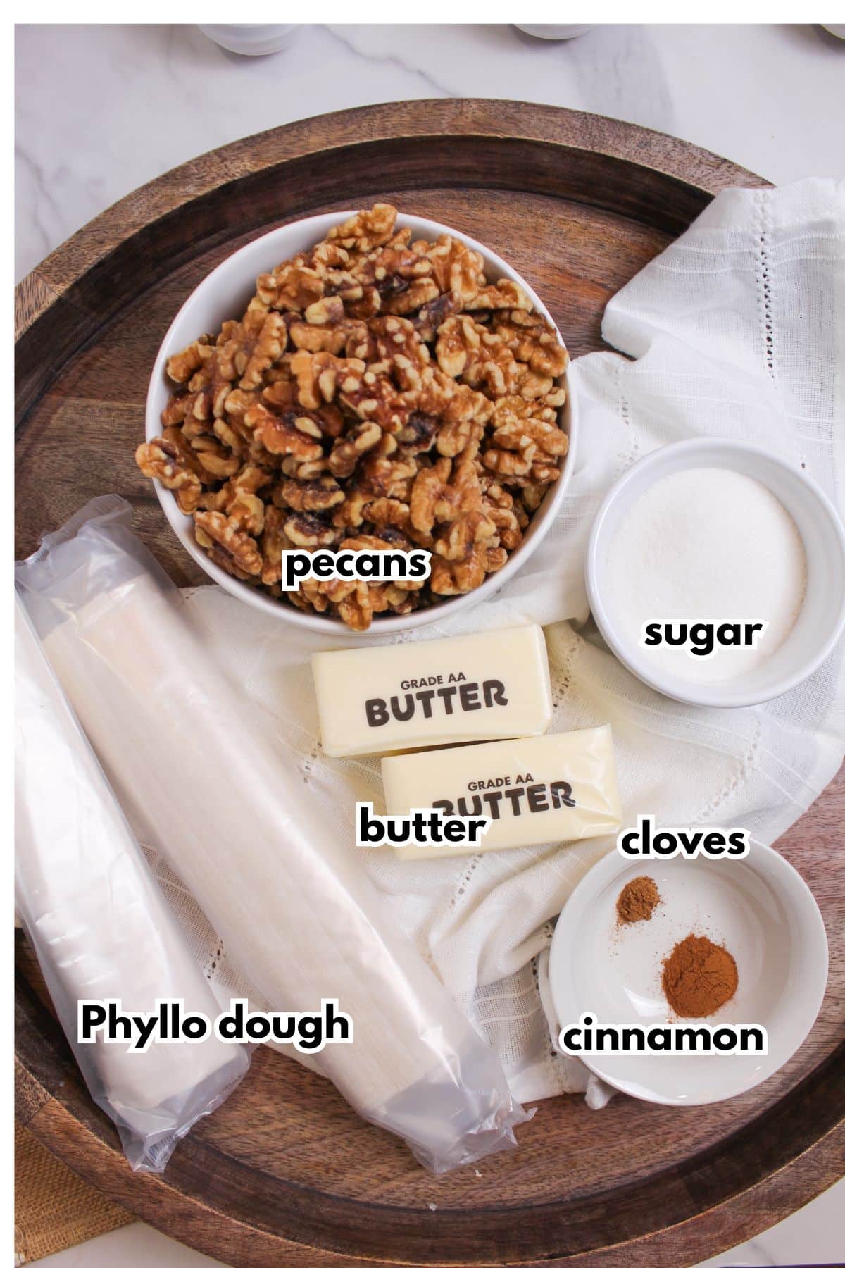 bowls of pecans, butter, sugar, cloves, cinnamon, and phyllo dough on a wooden serving tray.
