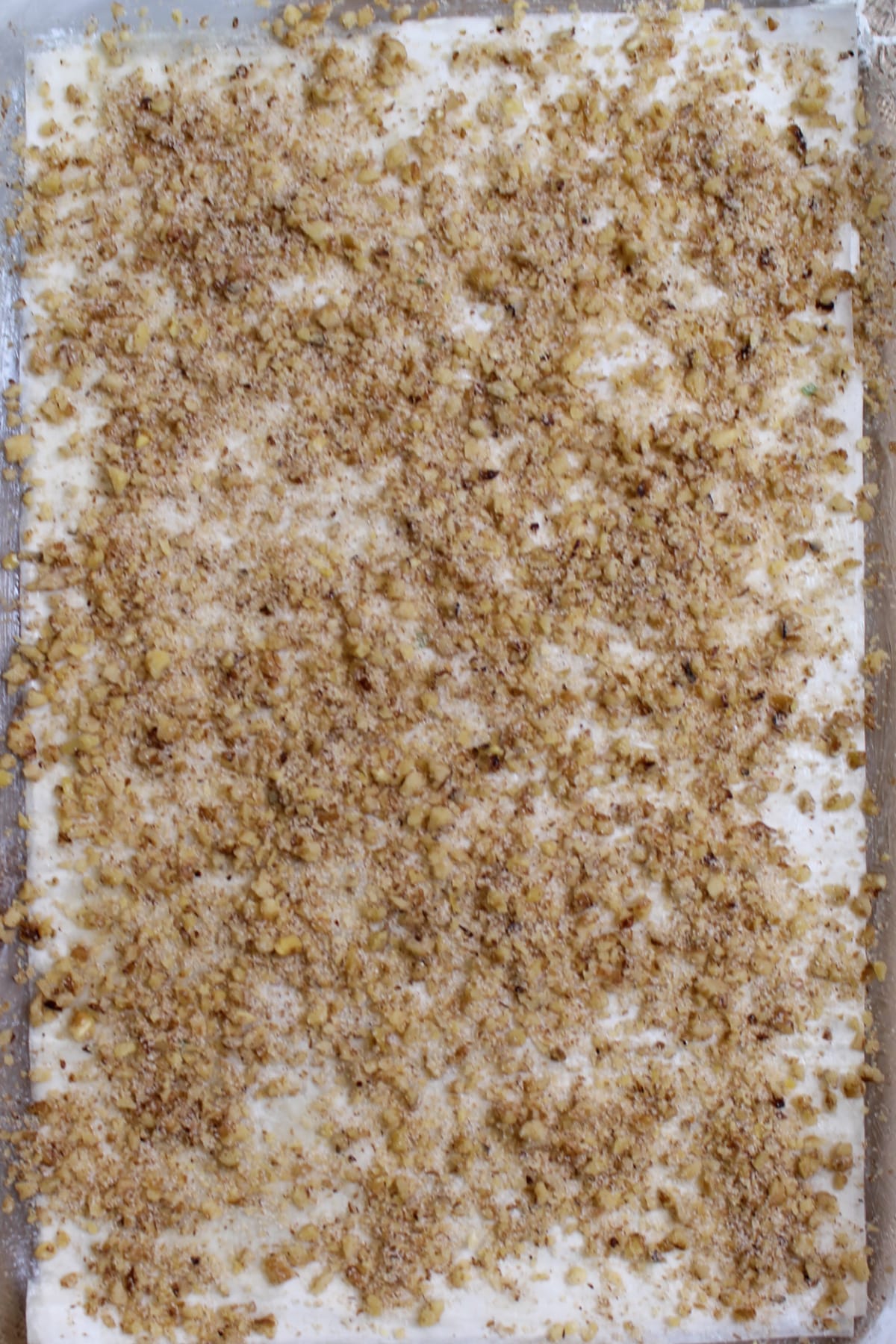 phyllo dough and pecan layer being layered in a baking dish.