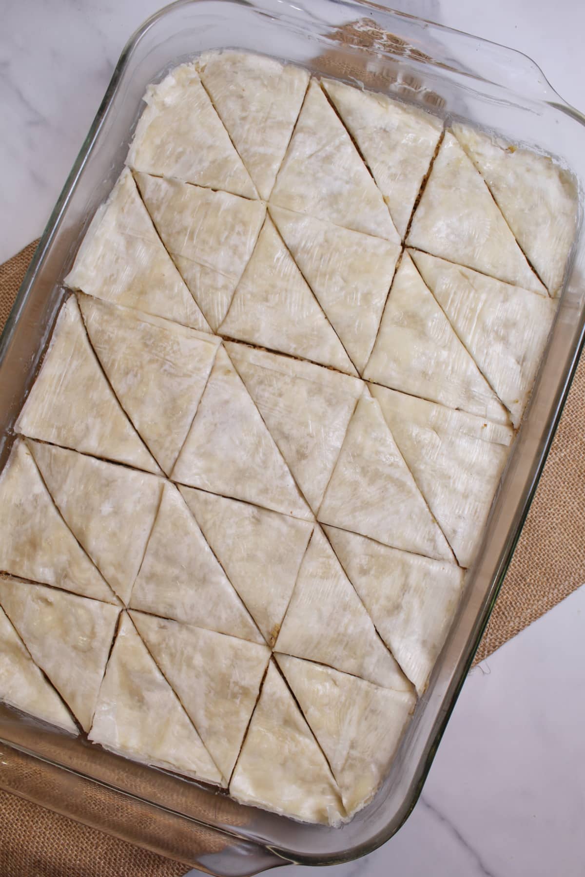 raw baklava cut into squares in a glass baking dish.