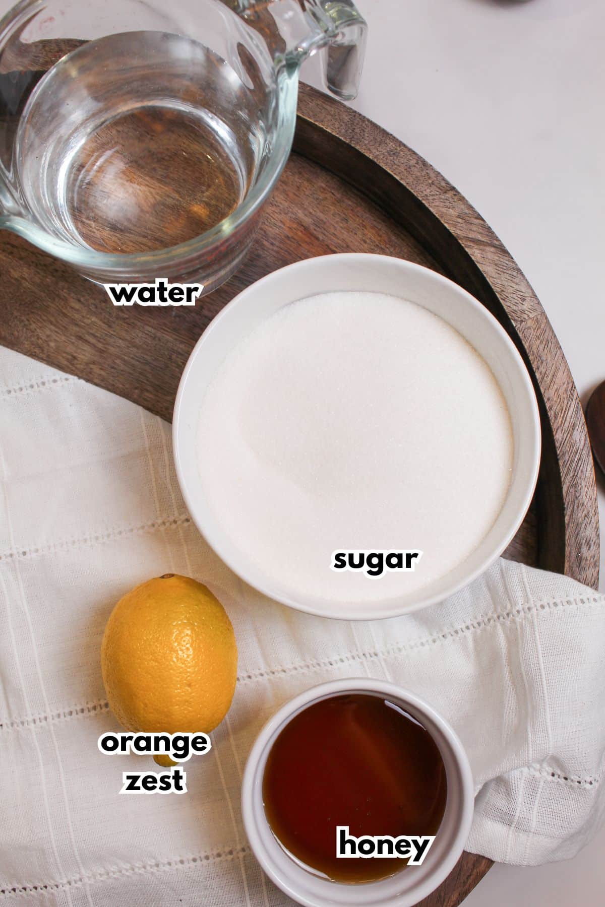 bowls of water, sugar, honey, and orange zest on a wooden serving tray.