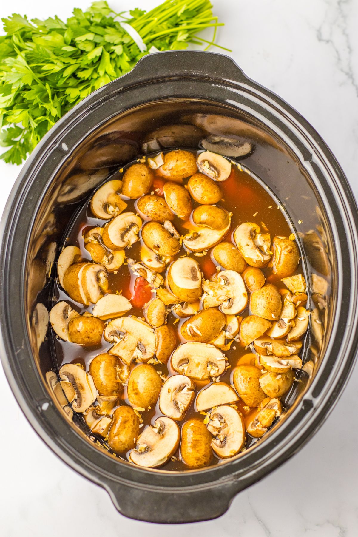 mushrooms, beef, and other soup ingredients in a slow cooker.