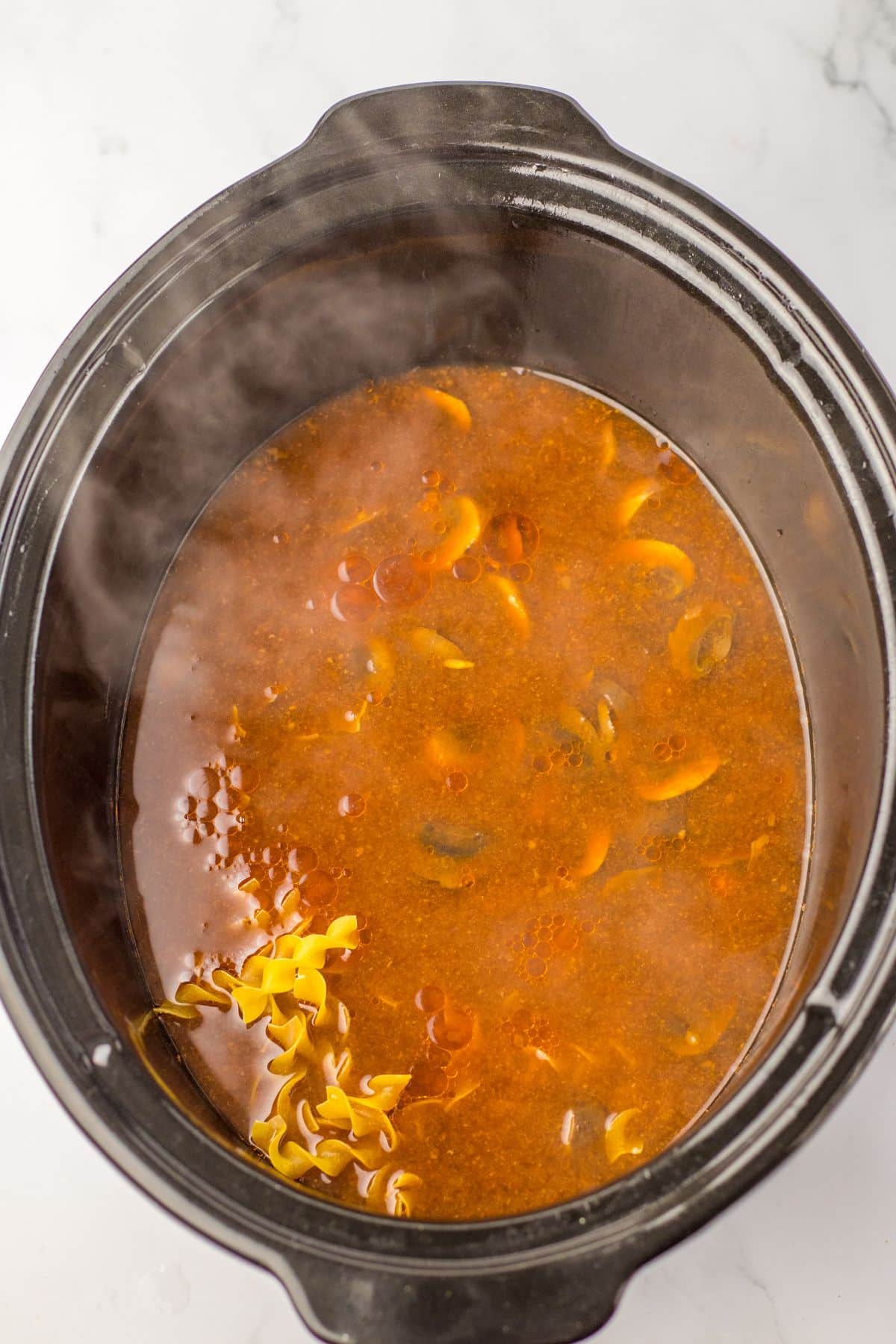 raw noodles being added to a slow cooker full of soup.
