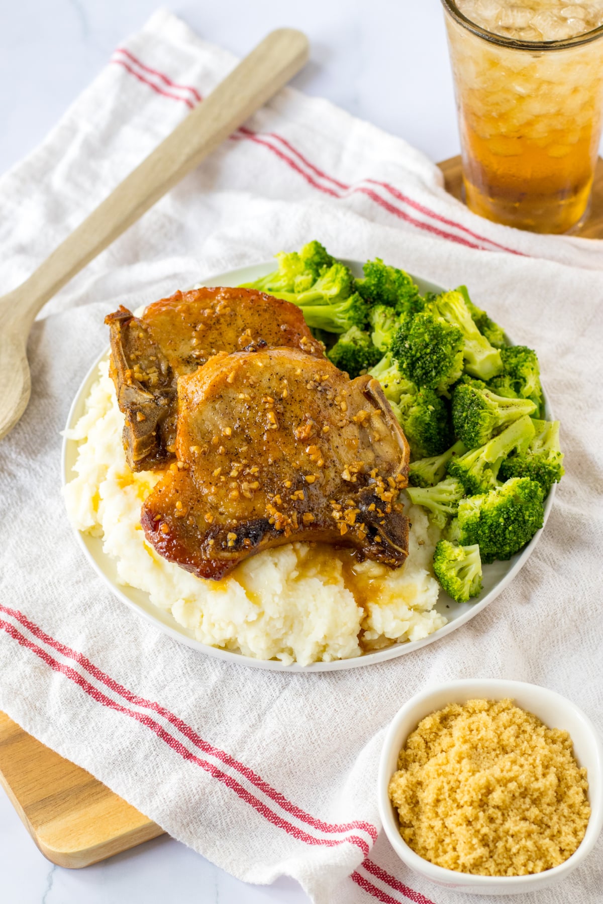 two slow cooker brown sugar pork chops on a plate with mashed potatoes and broccoli.