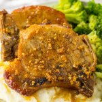 two slow cooker brown sugar pork chops on a plate with mashed potatoes and broccoli.