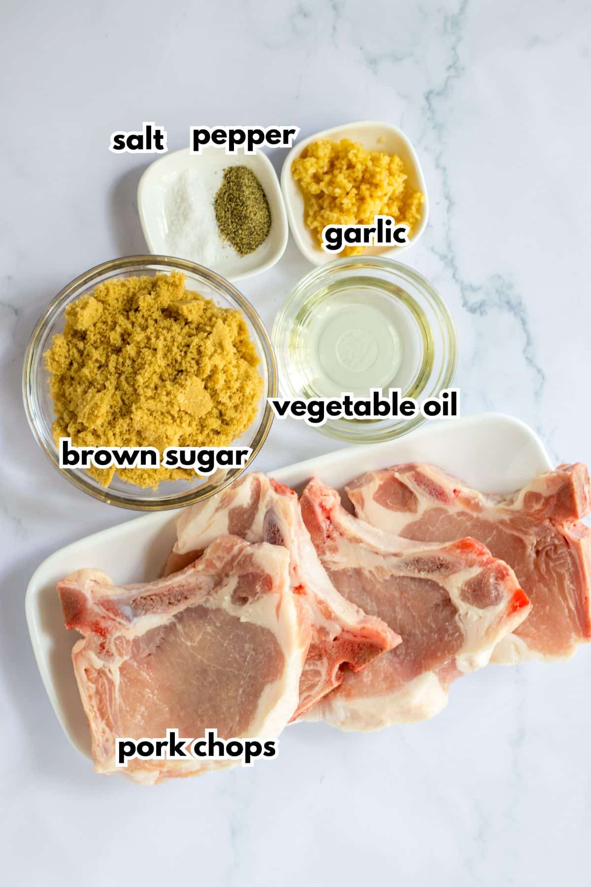 bowls of salt, pepper, minced garlic, brown sugar, vegetable oil, and raw pork chops.