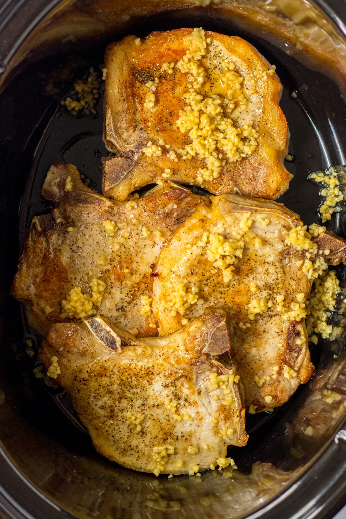garlic on top of seared pork chops in a slow cooker.