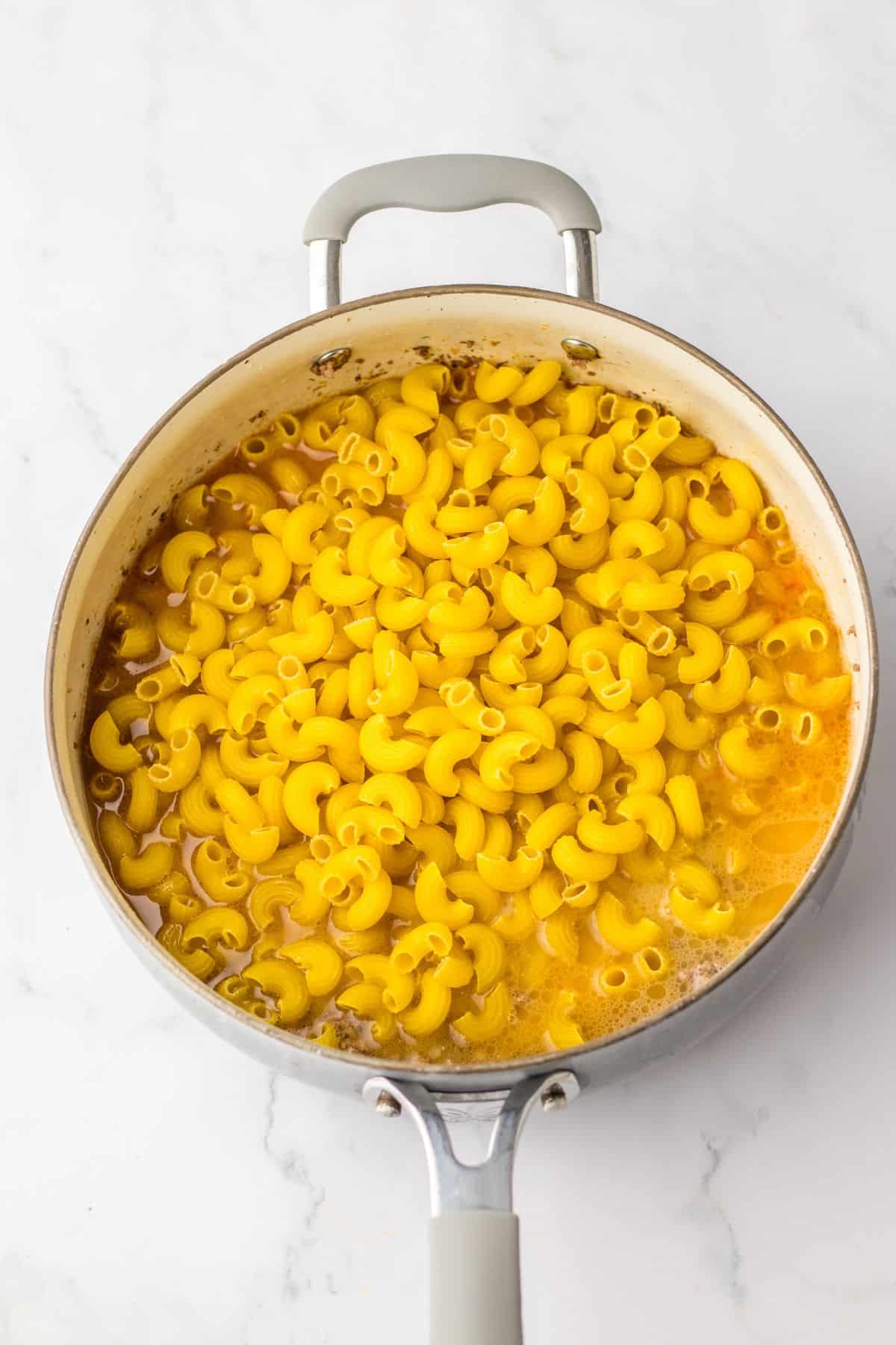 raw noodles being added to ground beef and sauce mixture in a skillet.