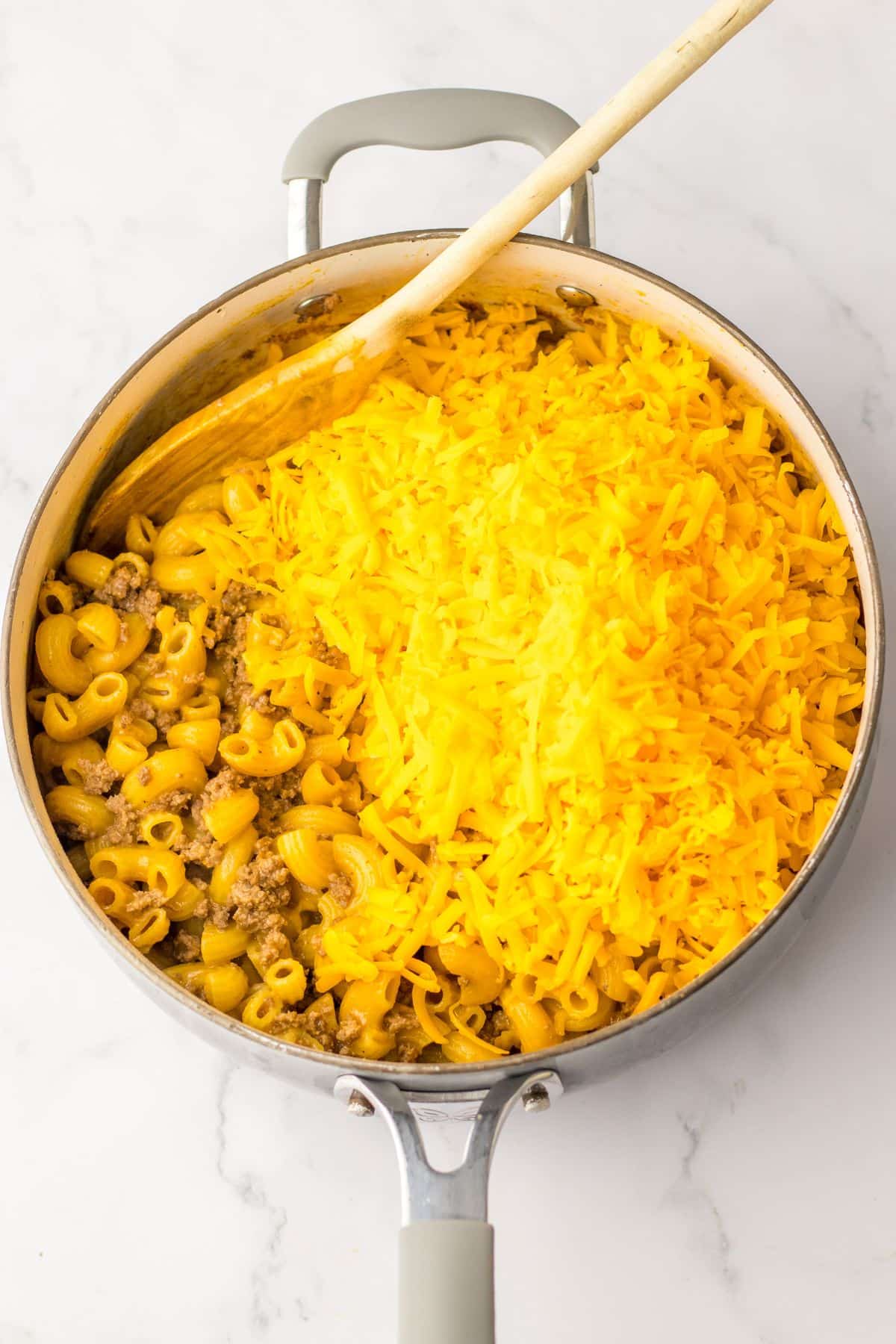 shredded cheese being added on top of a pasta in a skillet.