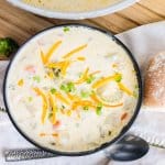 bowl filled with cheesy potato soup and topped with shredded cheese and sliced green onions.