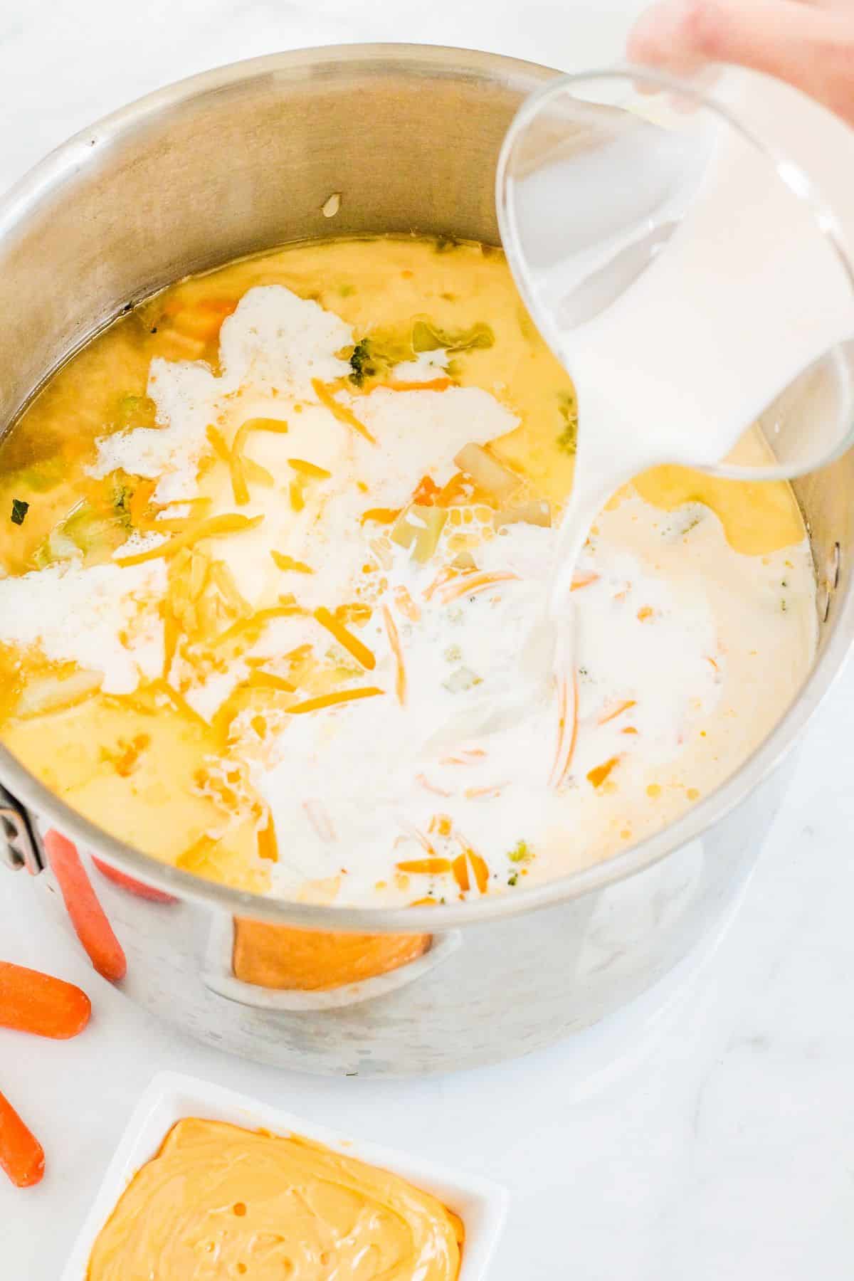 half and half being poured in a sauce pan filled with vegetables.