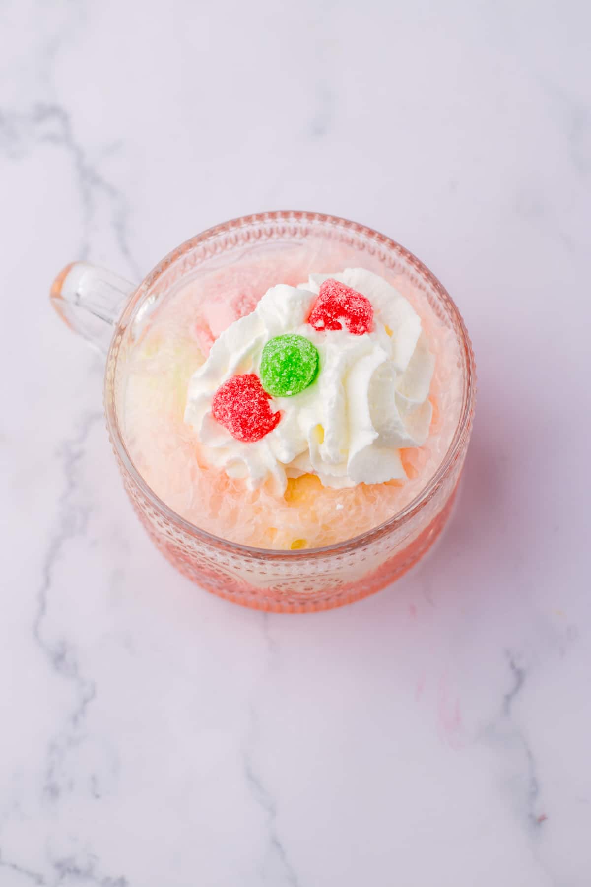 whipped cream and gumdrops on top of a cherry punch in a glass mug.
